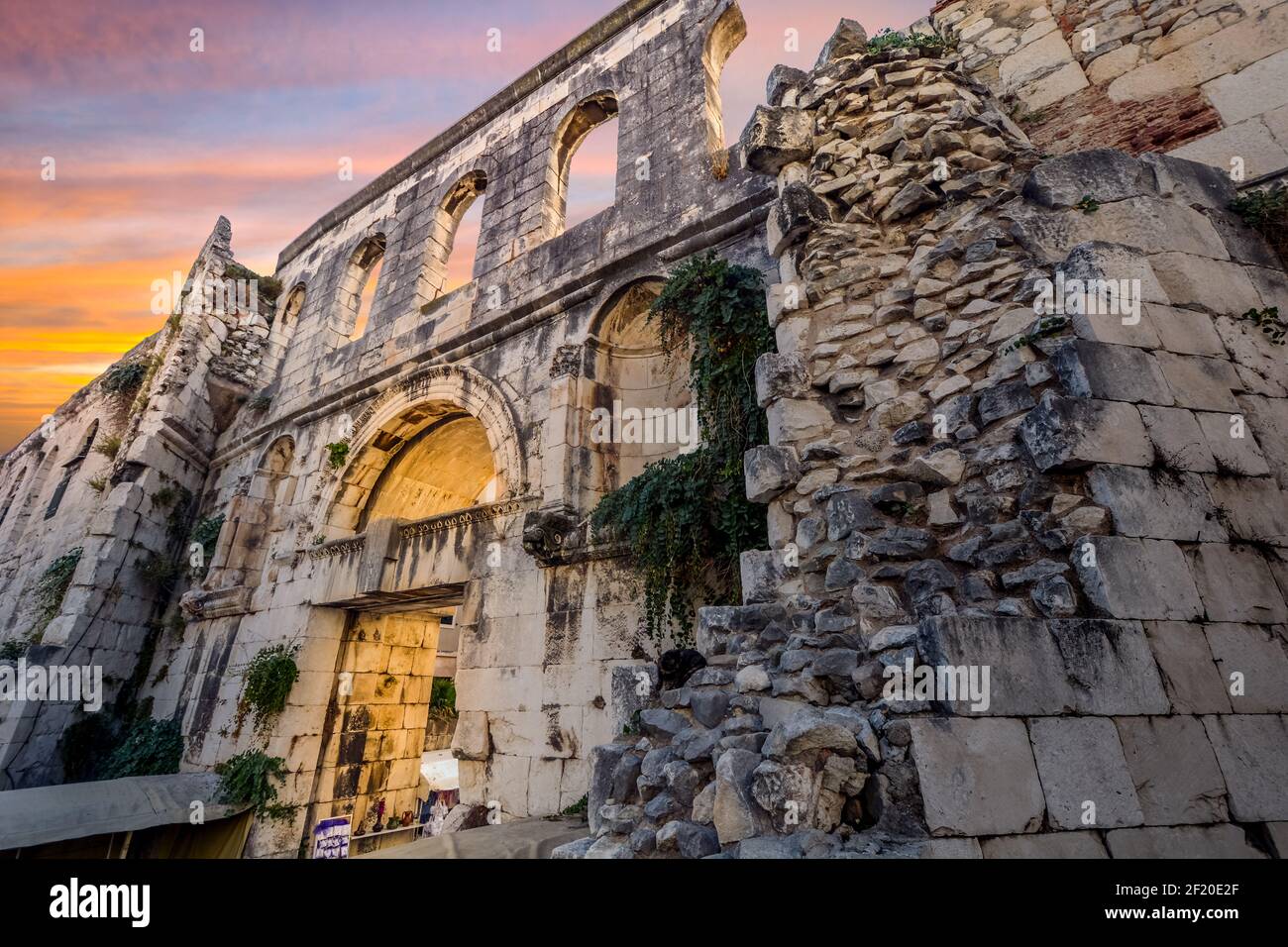 Un gato se encuentra sobre piedras apiladas cerca de la Puerta de Plata del antiguo Palacio del Emperador Diocleciano en las ruinas romanas de la ciudad antigua en Split, Croacia, al atardecer. Foto de stock