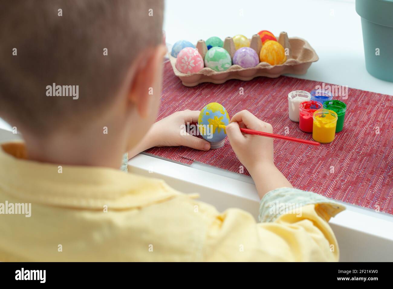 Creadora Caucásica niño pintando huevos de Pascua. Niño preescolar decorar y pintar huevos de pascua en diferentes colores. Preparación para la fiesta EAS Foto de stock