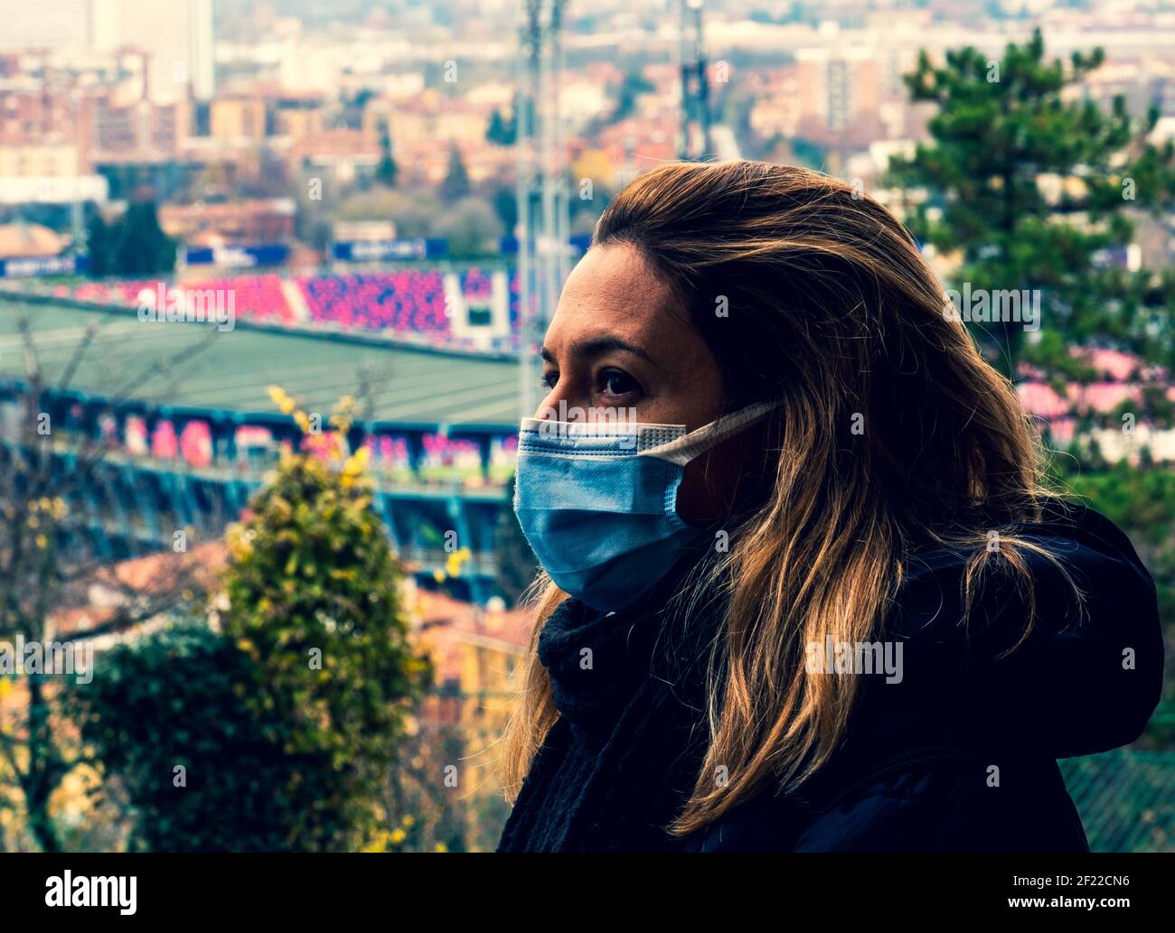 mujer con máscara en la vista de perfil de la cara preocupada por el coronavirus pandemia con vistas a una ciudad y estadio en el antecedentes Foto de stock
