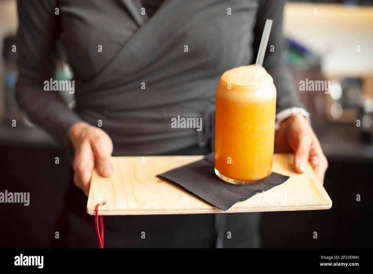 Primer plano de la camarera, con las manos sosteniendo un vaso de zumo de naranja fresco en la bandeja. Concepto de estilo de vida saludable Foto de stock