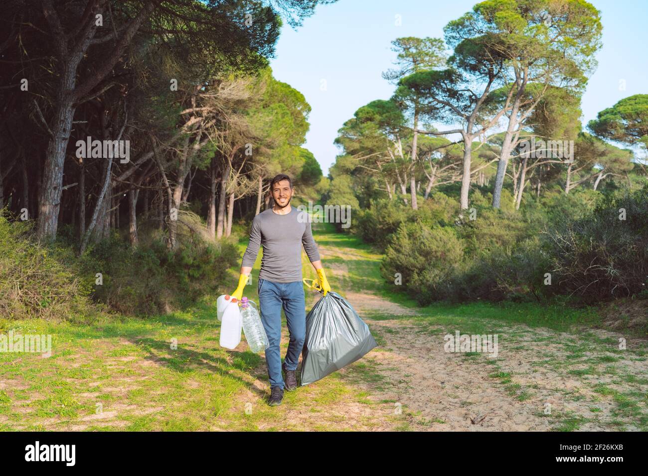 Hombre voluntario con bolsa de basura limpiando el bosque de plástico contaminación Foto de stock
