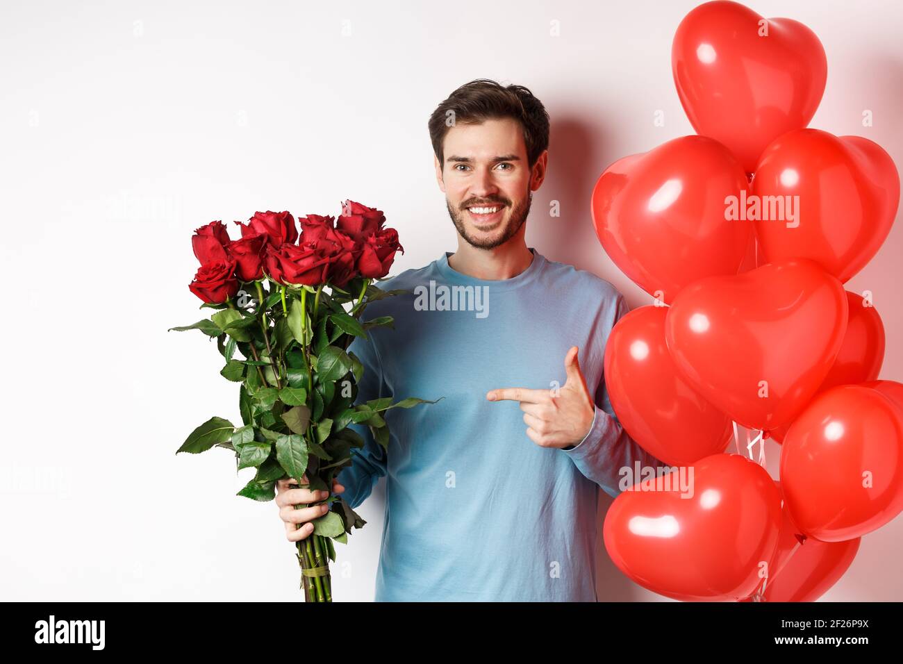 Día de San Valentín romance. Feliz joven con flores y globos de corazón que  van a la fecha con el amante. Un hombre sonriente que apunta al bouque  Fotografía de stock -