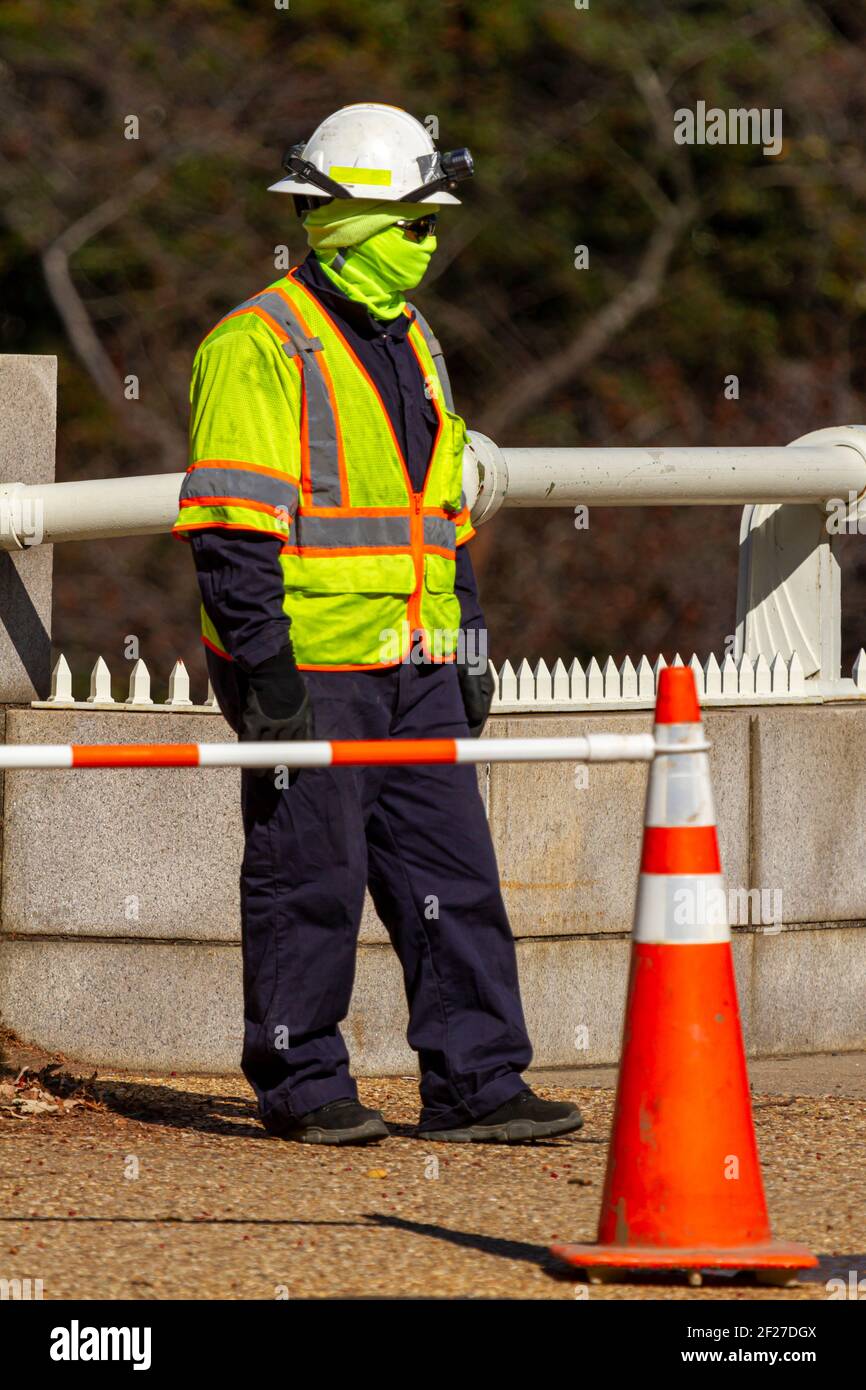 Se ve a un trabajador de la construcción que lleva todo el equipo protector incluyendo casco, chaleco reflectante, botas, guantes, gafas de sol y máscara facial contra COVID-19 Foto de stock