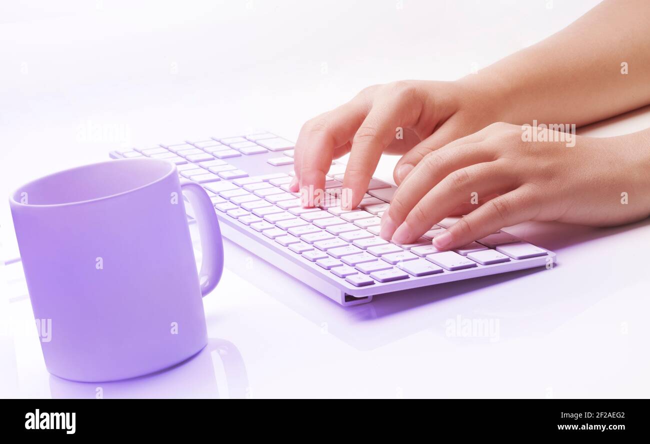 Mujer manos escribiendo en un teclado y una taza de café sobre fondo blanco. Tema colorido. Color suave de contraste. Foto de stock