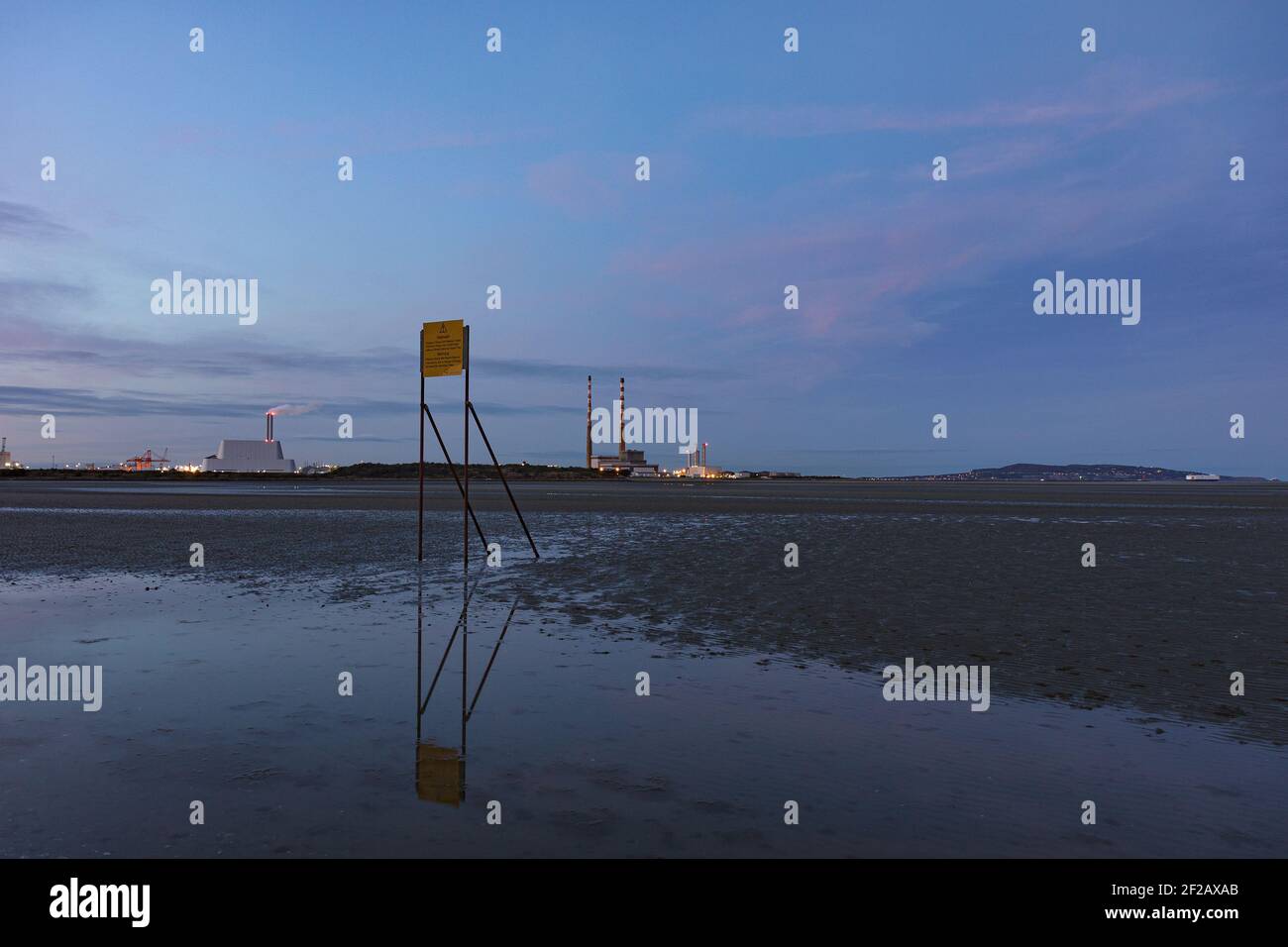 Sandymount, playa de Dublín al atardecer, señal de advertencia sobre la marea que viene rápidamente, chimeneas Poolbeg y incinerador en el fondo Foto de stock