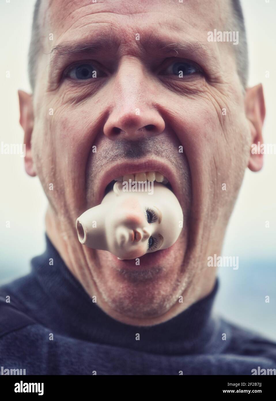 Hombre medio adulto con expresión facial conmocionada y sosteniendo la cabeza de la muñeca en su boca. Concepto alarmado, conmocionado, asustado Foto de stock