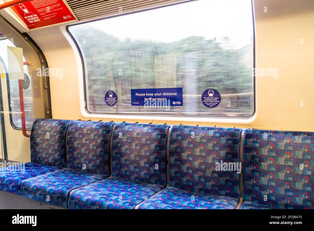 Vista a través de la ventana de una línea central de Londres vacía Tren subterráneo con una cara de coronavirus que cubre la señal de advertencia Foto de stock