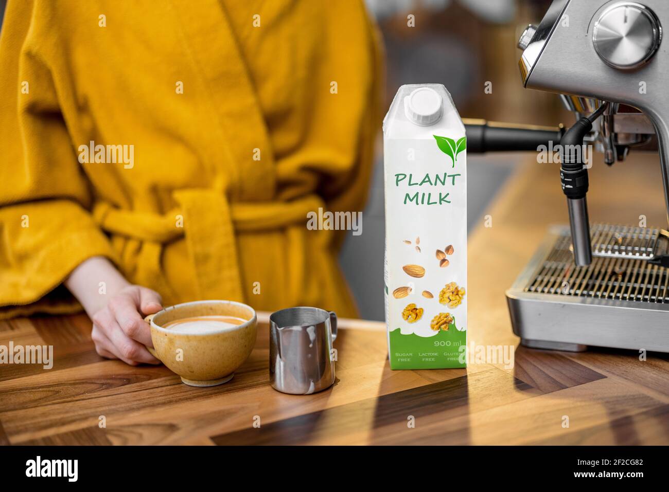 Mujer en un albornoz amarillo haciendo capuchino con leche de planta en una  máquina de café profesional por la mañana en casa. Envasado de leche  vegetal cerca del café Fotografía de stock -