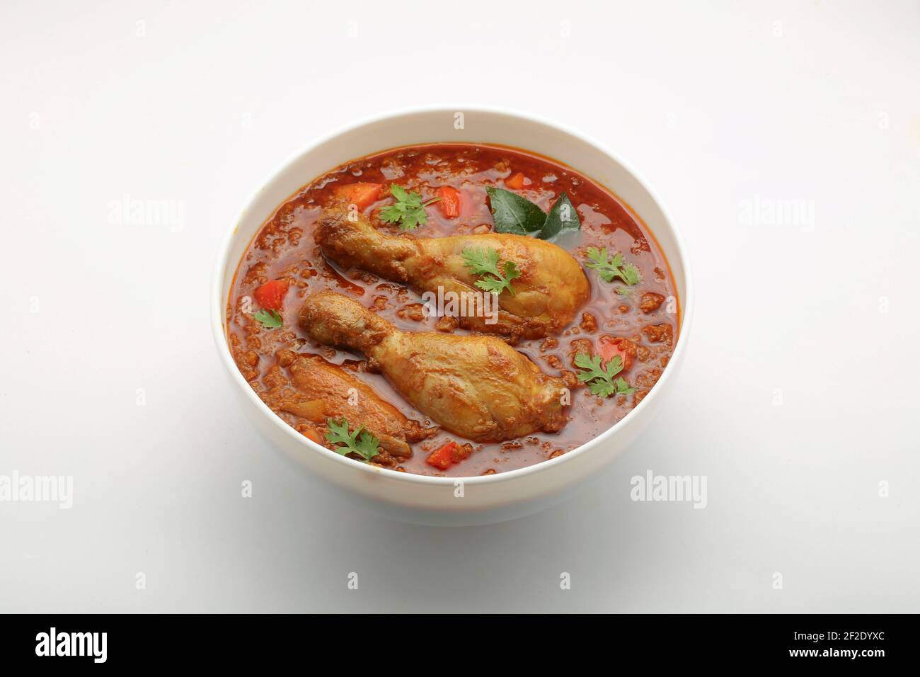 Curry de pollo o masala, plato picante de pata de pollo rojizo adornada con hoja de cilantro y Chile verde fresco. Foto de stock