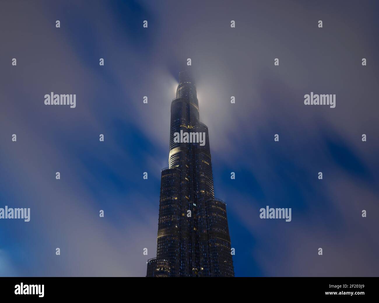 Burj Khalifa por la noche con la parte superior cubierta por nubes bajas. Rascacielos en Dubai, Emiratos Árabes Unidos. La cima de gran altura detrás de la nube. Foto de stock