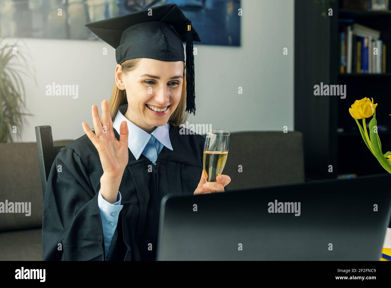 fiesta de graduación de distanciamiento social - graduada femenina con vestido y celebre su licenciatura en línea con amigos de la universidad en casa Foto de stock