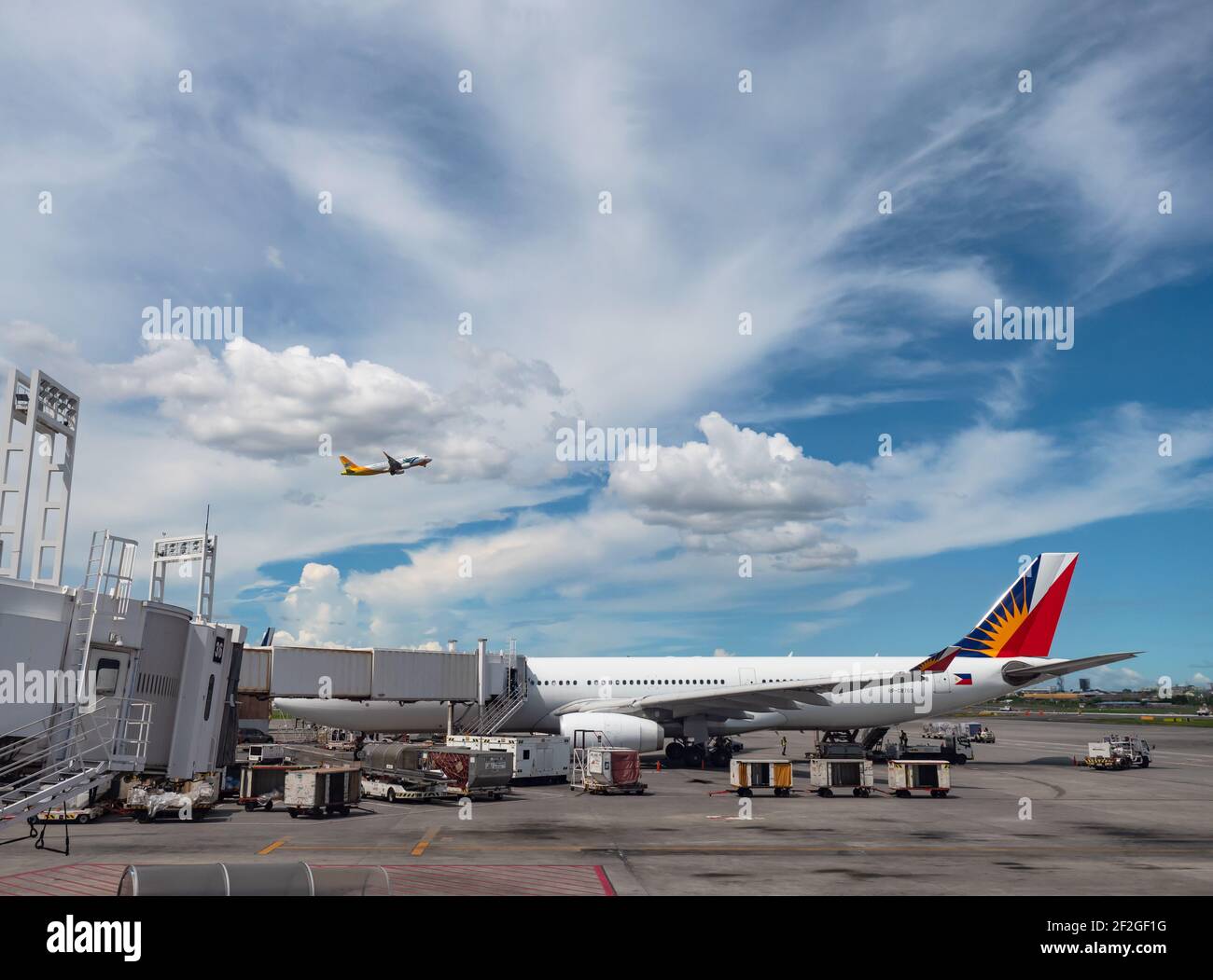 Philippine Airlines Airbus A330 en la Terminal 2 del Aeropuerto Internacional Ninoy Aquino en Manila, con Cebu Pacific Airbus A320 volando por encima. Foto de stock