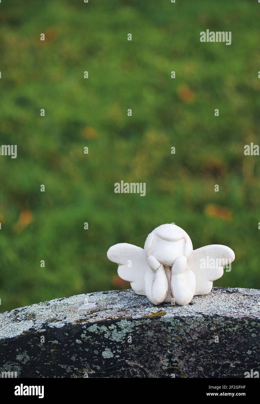 Pequeña escultura de ángel alado blanco sin rostro con la cabeza en las manos encima de la lápida. Concepto de recuerdo, muerte, espiritualidad Foto de stock