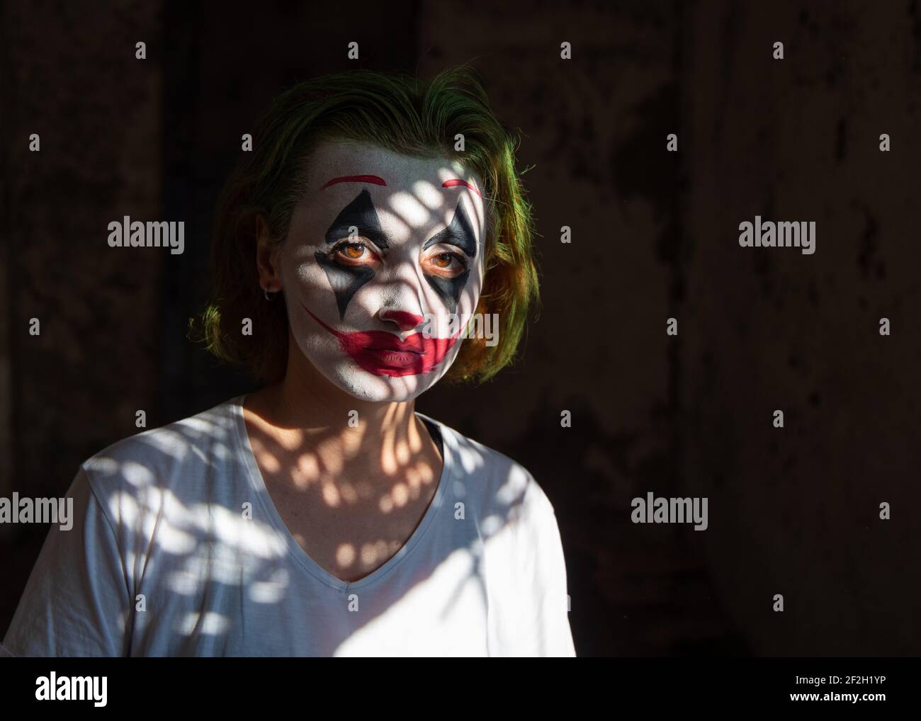 Primer plano Retrato de atractiva joven con la pintura de la cara como Joker, payaso contra fondo negro, gente. Foto de stock