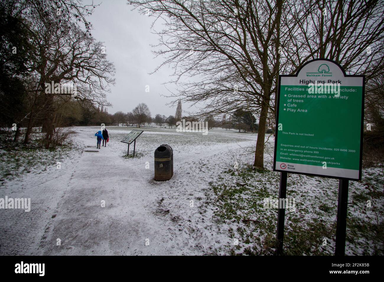 Highams Park Londres, el Highams Park en Highams Park, Londres durante la nieve de invierno, con gente caminando entre los árboles y cartel en primer plano Foto de stock