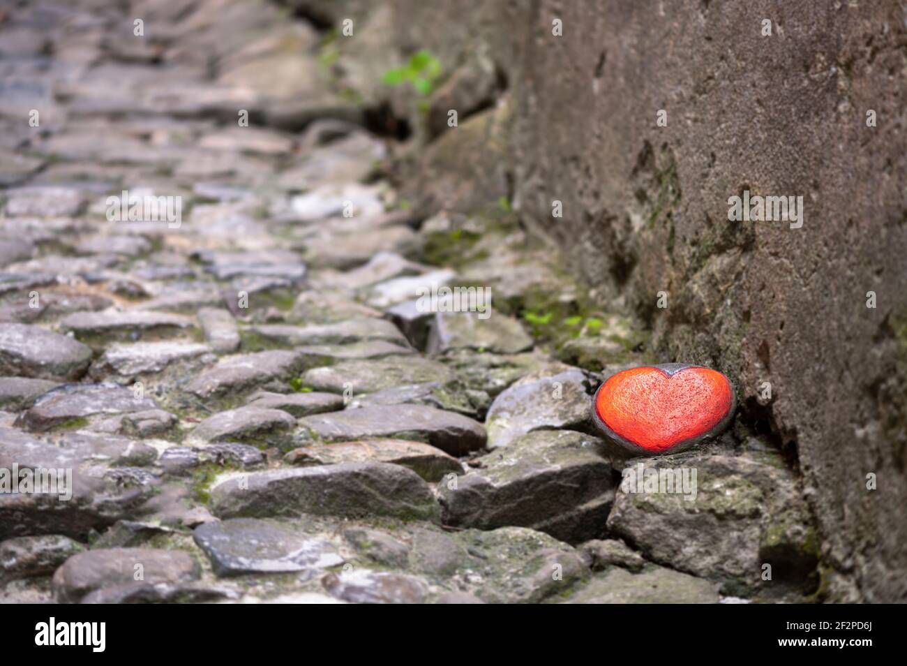 Piedra pintada con un corazón rojo en un camino pavimentado, símbolo de la calidez del corazón contra la frialdad en las relaciones Foto de stock