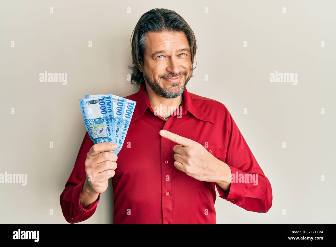 Hombre guapo de mediana edad con 1000 billetes de forint húngaros sonriendo feliz señalar con la mano y el dedo Foto de stock