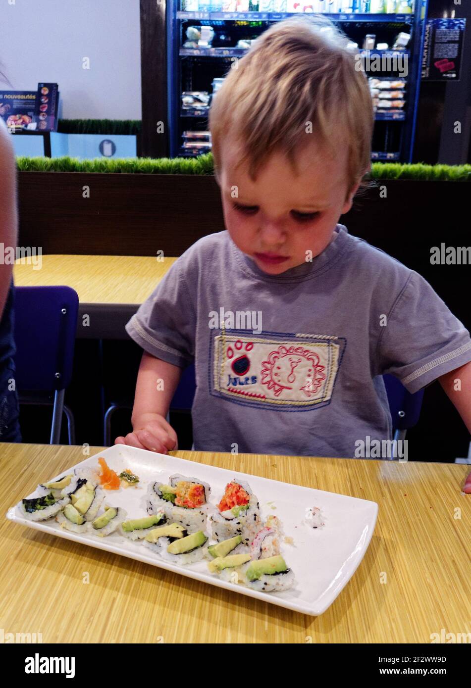 Un niño pequeño (2 años) mirando sospechosamente un plato de sushi en un restaurante Foto de stock