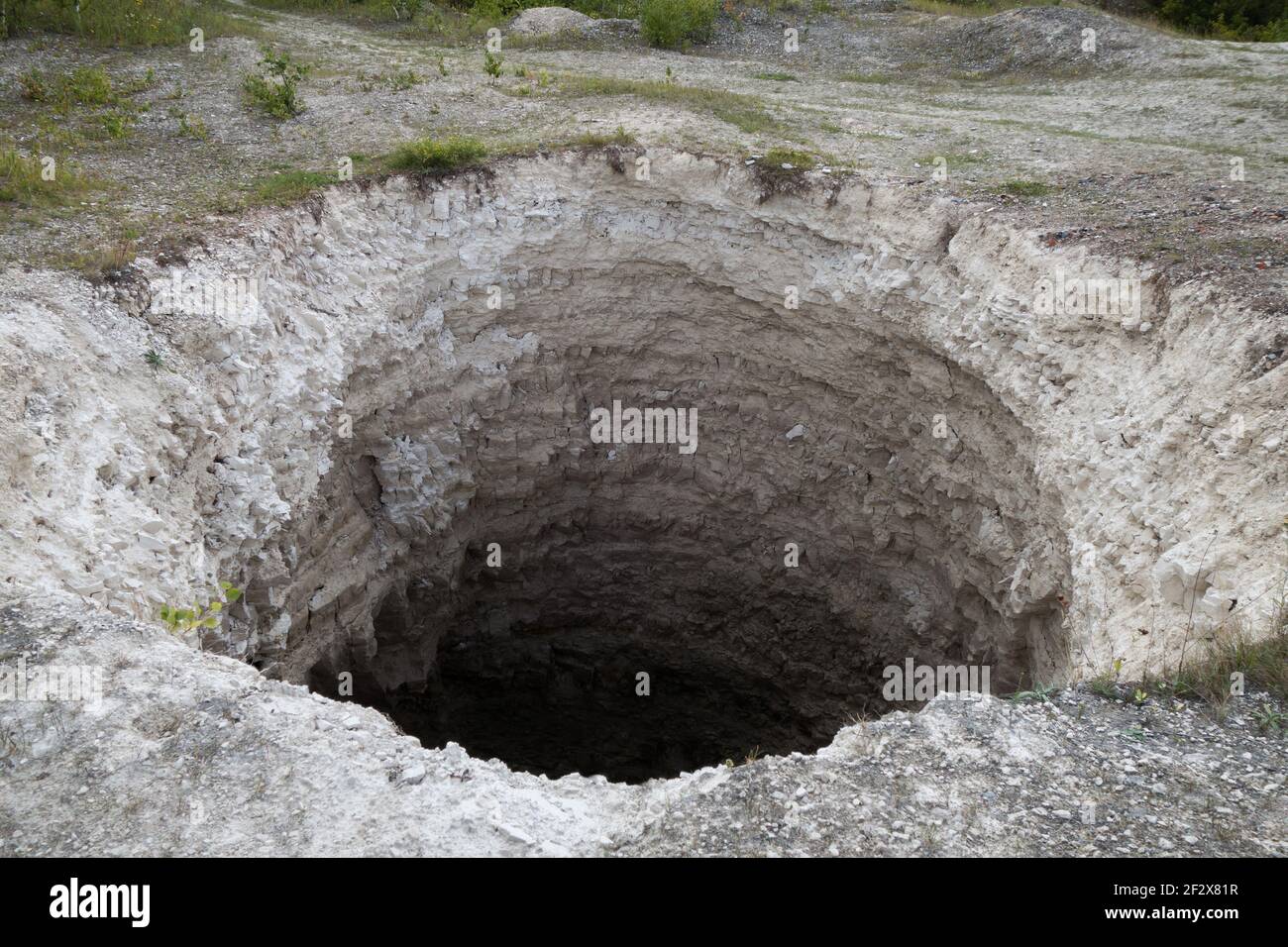 Abertura negra del agujero de karst, formado sobre la mina de piedra caliza abandonada. Diámetro de unos 15 pies, profundidad de unos 40-50 pies. El proceso de formación sigue en curso Foto de stock