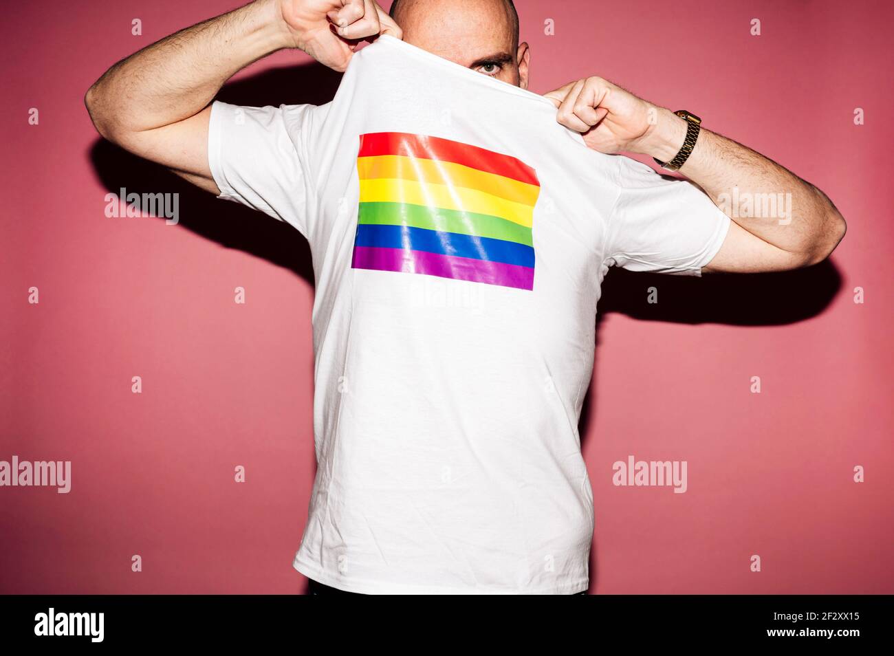 Crop anónimo joven homosexual masculino cubrir cara con t camisa con  bandera arcoiris y mirando la cámara Fotografía de stock - Alamy
