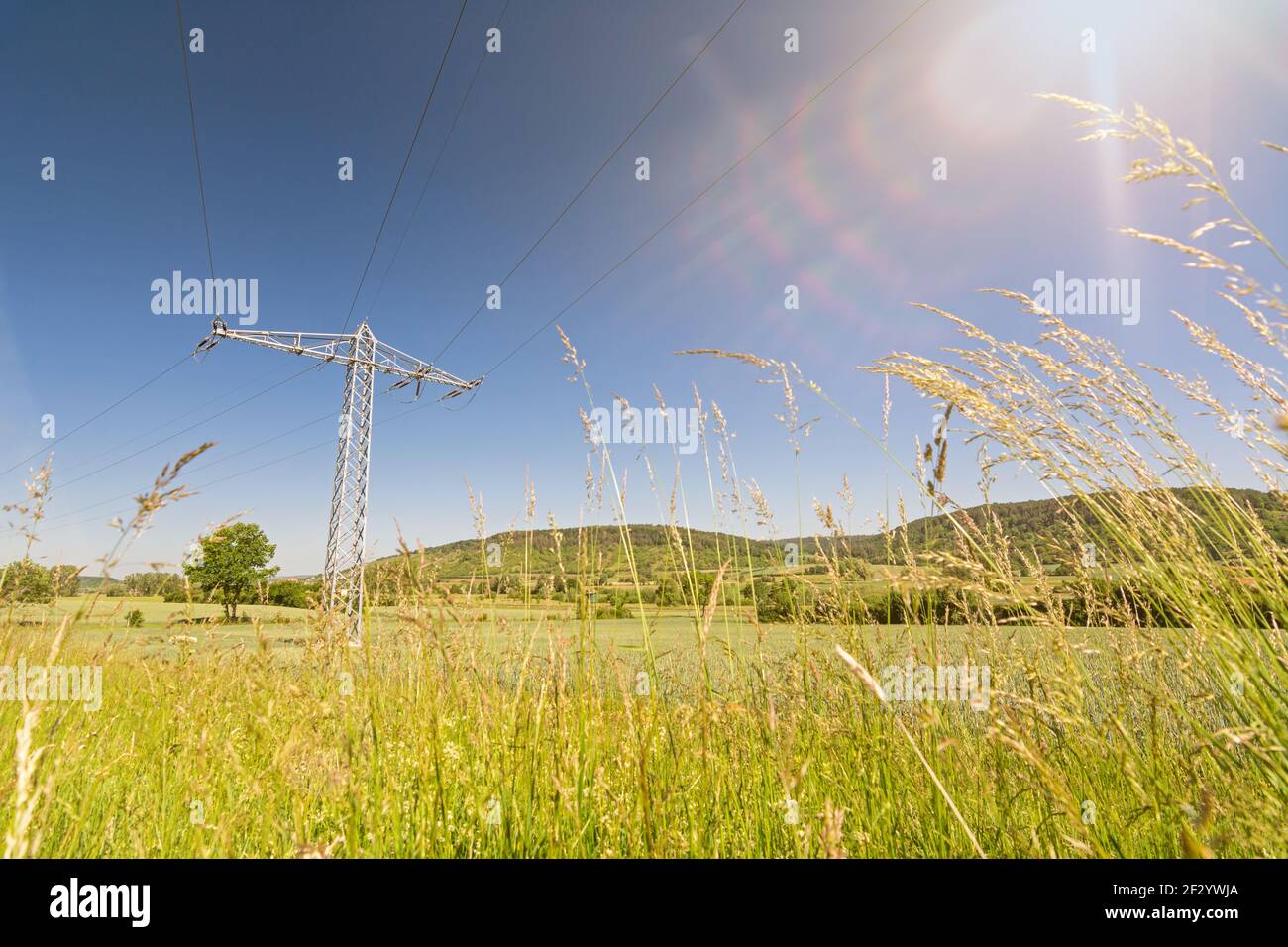 Pilón de electricidad y rayos solares en un campo que simboliza el verde electricidad y energía renovable Foto de stock