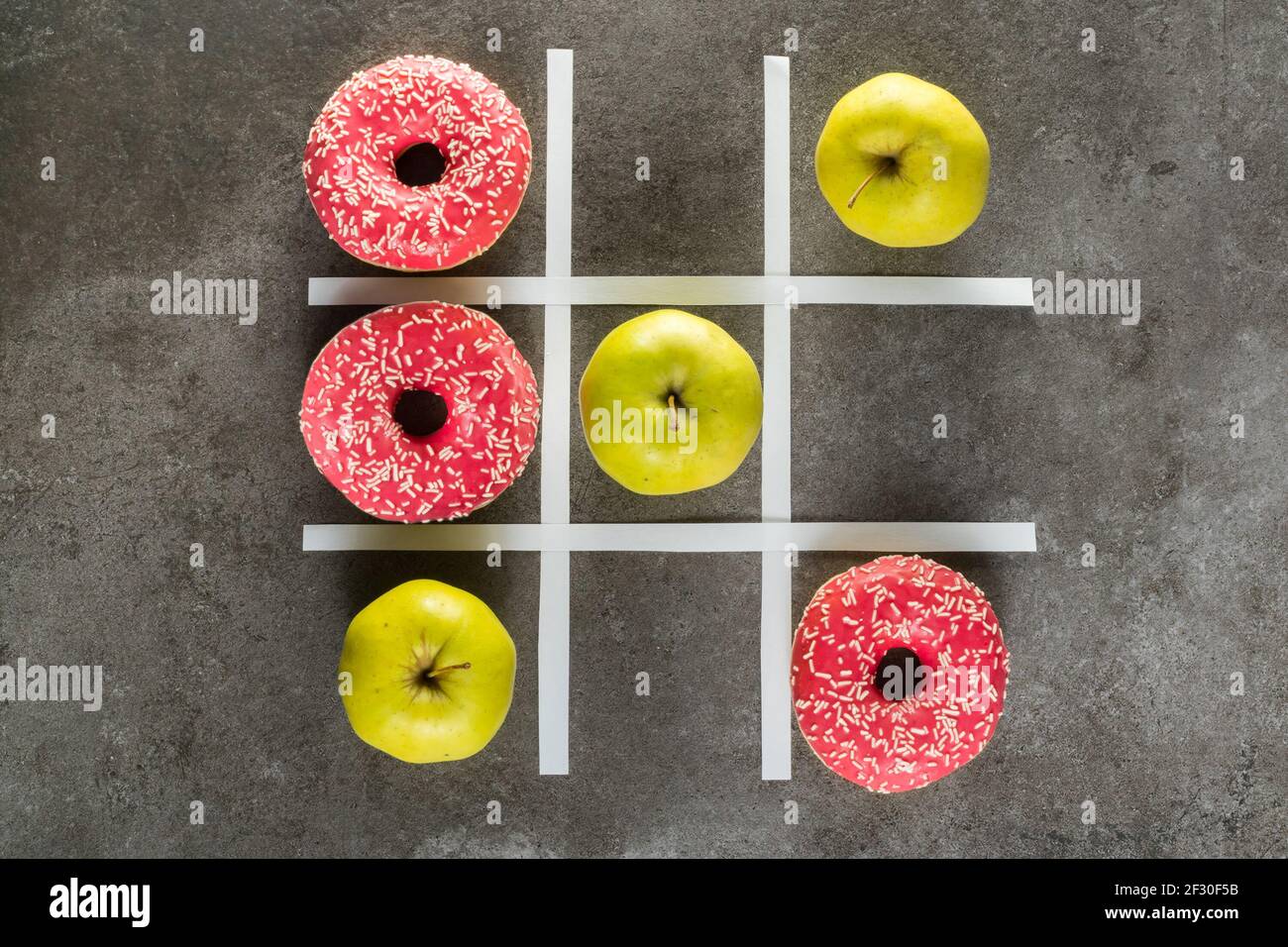 Comida sana vs malsana, manzanas verdes vs donuts en TIC tac juego de dedo del pie Foto de stock