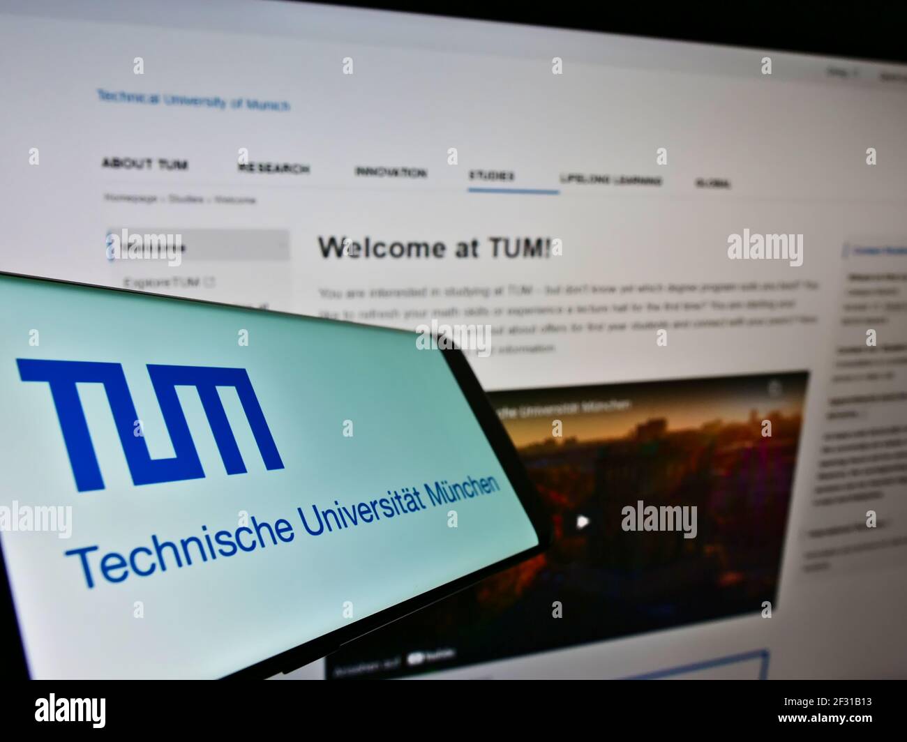 Teléfono móvil con el logotipo de la institución educativa alemana Technische Universität München en la pantalla frente a la página web. Enfoque en el centro de la pantalla del teléfono. Foto de stock