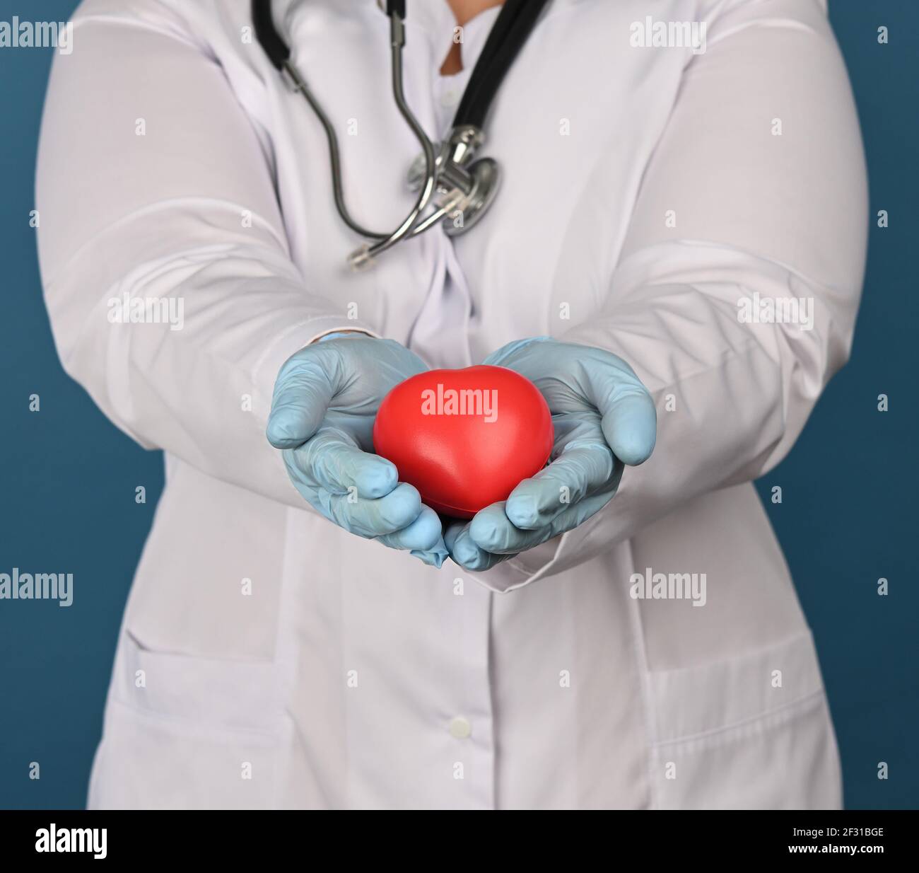 La mujer médica en un abrigo blanco sostiene un corazón rojo sobre un fondo azul Foto de stock