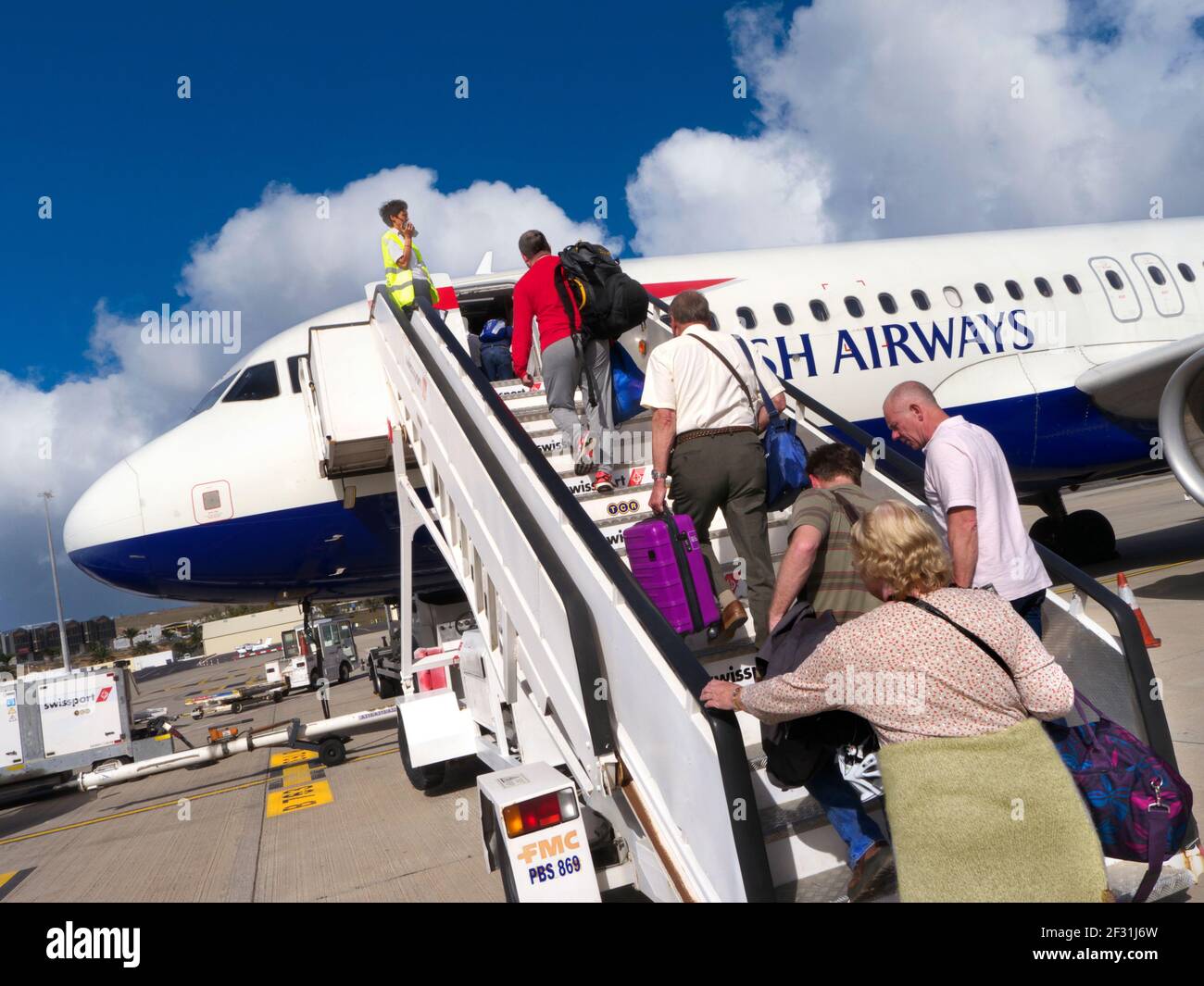 LOS PASAJEROS que embarquen en un avión de British Airways a través de los escalones de Cabina con equipaje de mano en el cielo azul de vacaciones soleado Airline concepto de