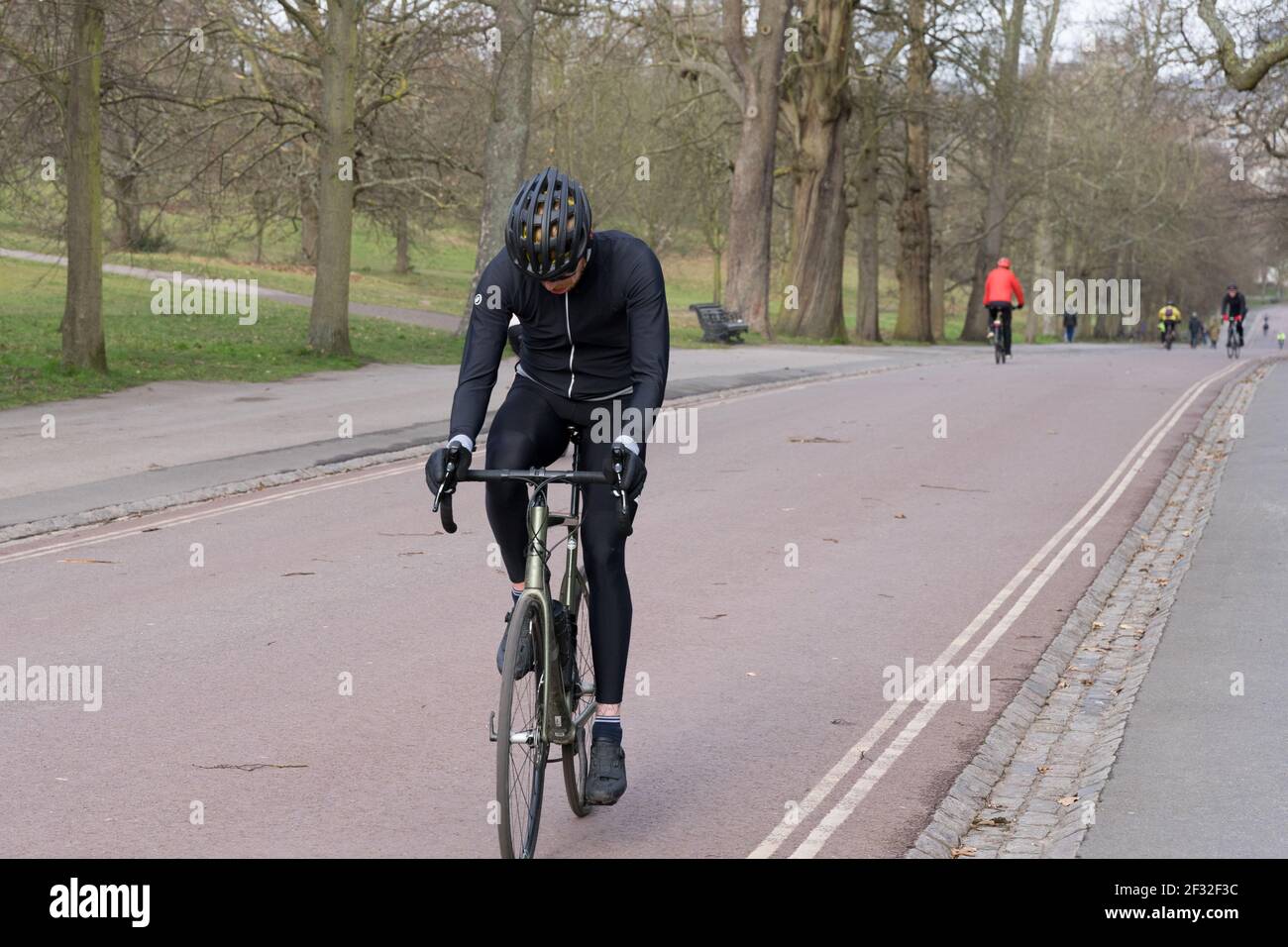 un hombre en la parte superior negra y el casco se monta en su bicicleta Cuesta arriba en el Greenwich Park de Londres para hacer ejercicio al aire libre Foto de stock