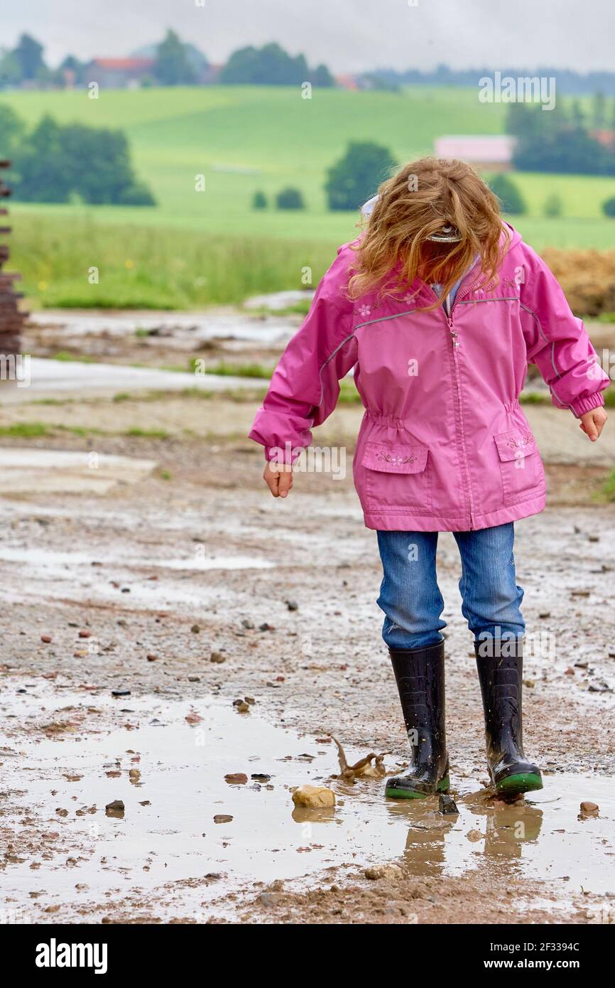 Chica de cuerpo entero en chubasquero rosa y botas de goma jugando en un  charco de barro en el campo Fotografía de stock - Alamy