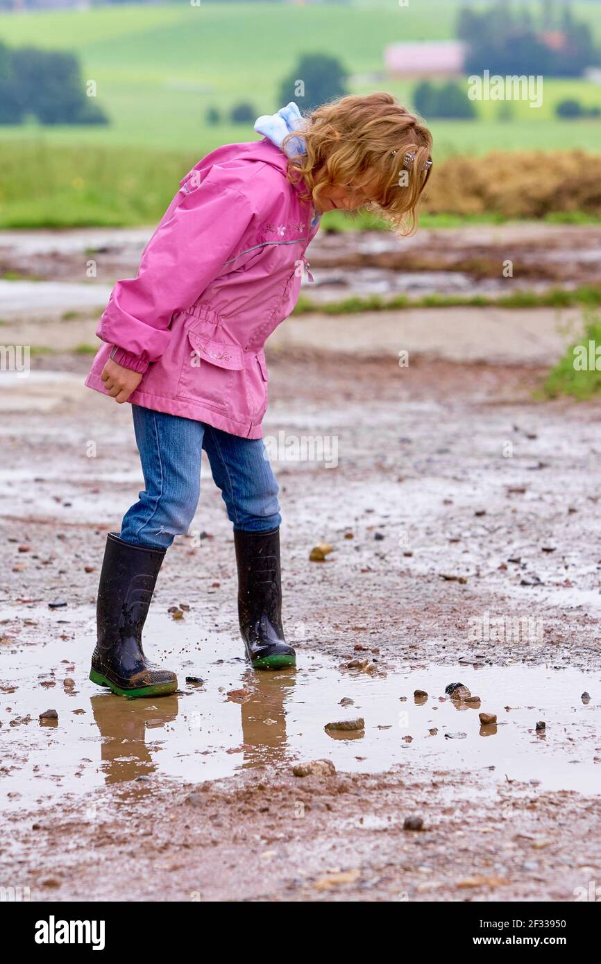 Chica de cuerpo entero en chubasquero rosa y botas de goma jugando un charco de barro en el campo Fotografía de stock - Alamy