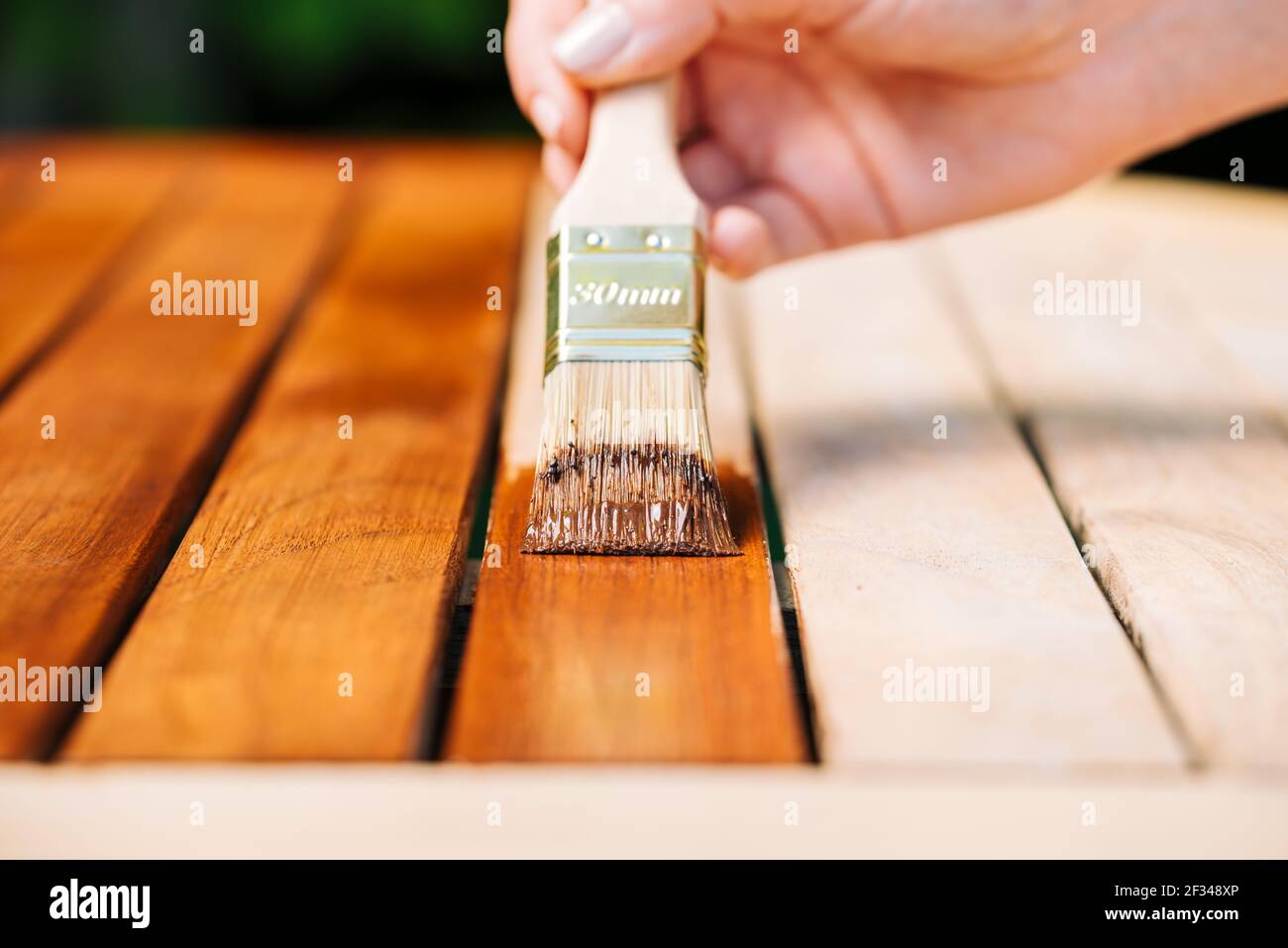 mano sosteniendo un pincel aplicando pintura barniz sobre una madera mesa  de jardín - pintura y cuidado de la madera con aceite Fotografía de stock -  Alamy