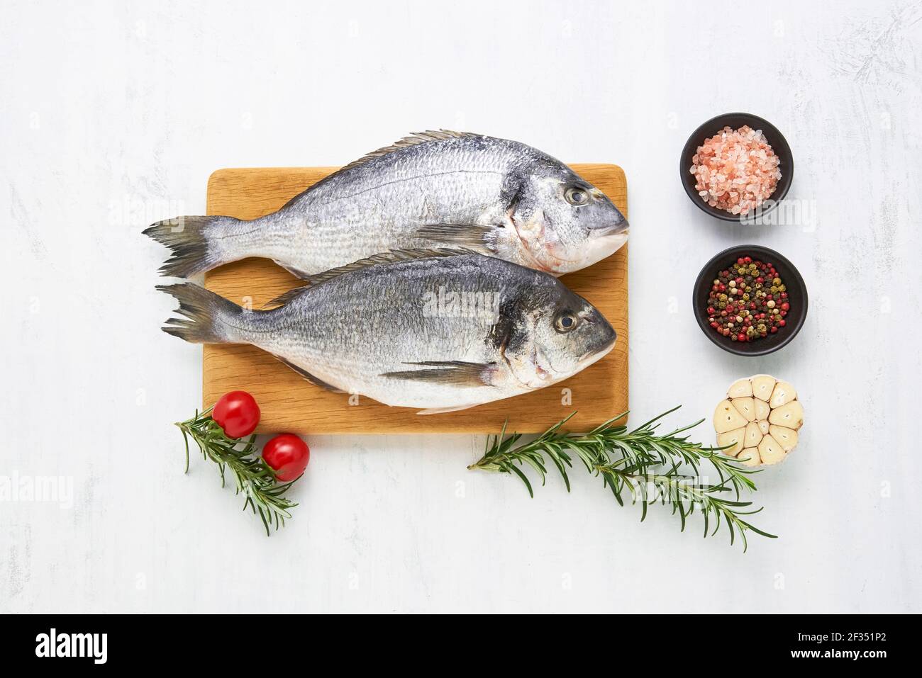 Pescado dorado crudo con especias sobre una tabla de madera sobre fondo blanco. Concepto de mariscos mediterráneos. Vista superior, espacio de copia para texto Foto de stock