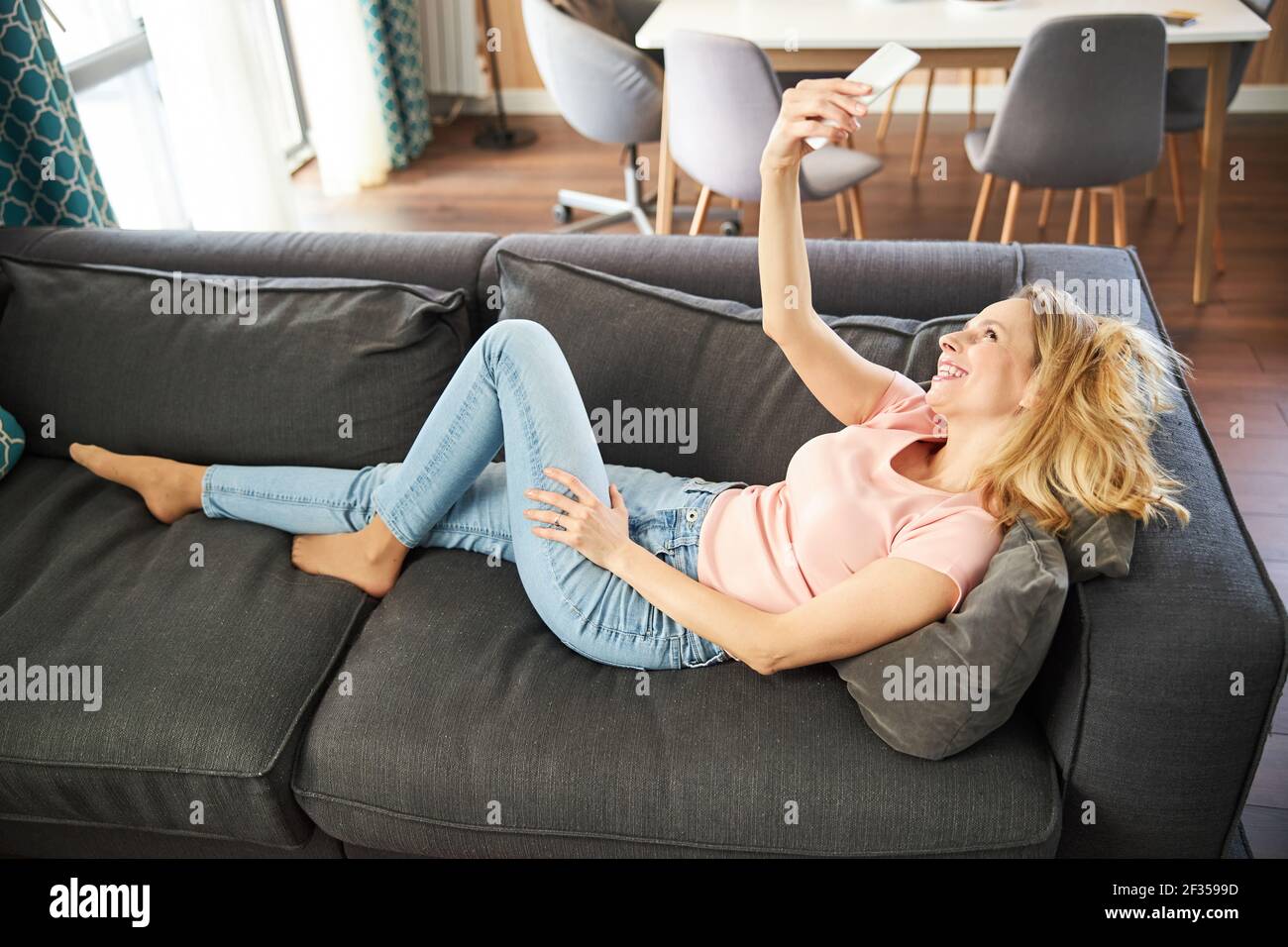 Mujer alegre acostada en el sofá y haciendo selfie en casa Fotografía de  stock - Alamy