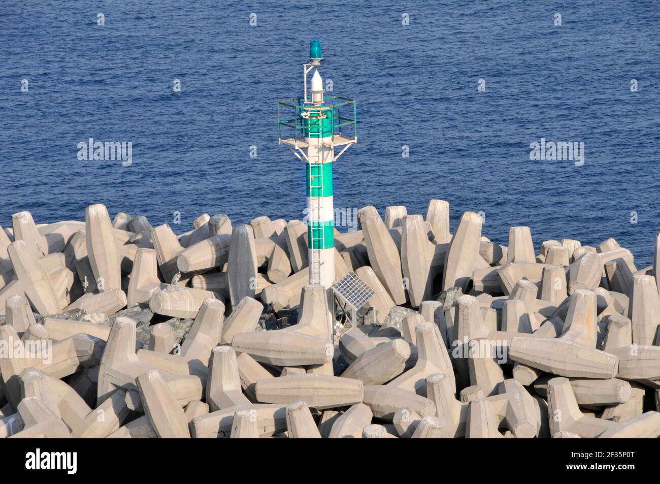 Bloques de hormigón prefabricado pesado tipo Dolosse en grandes pilas AS rompeolas protege el canal de navegación verde marcador de ayuda de la torre y advertir envíos Dubai UAE Foto de stock