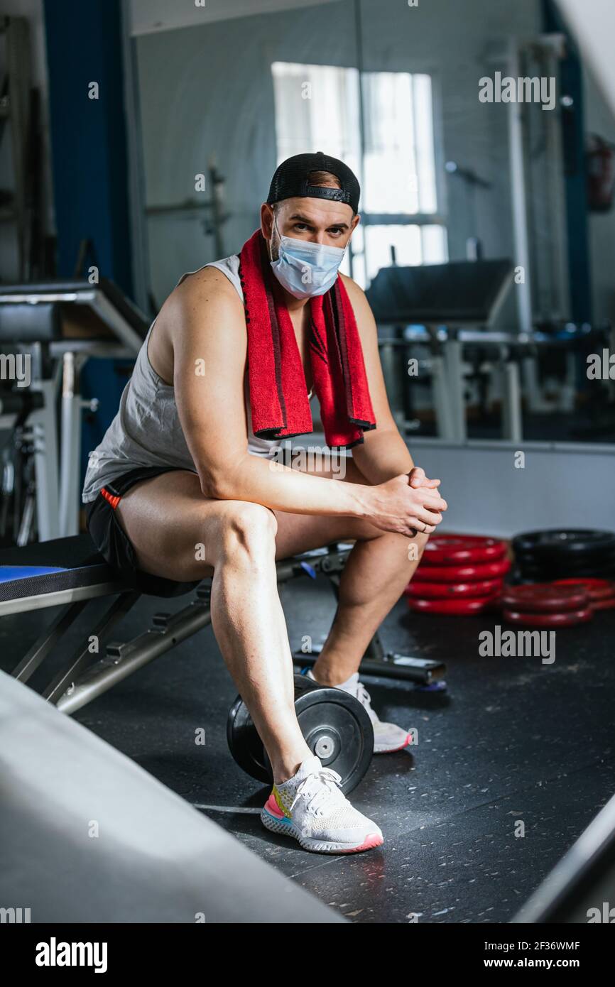 Hombre sentado en el gimnasio con una toalla alrededor del cuello. Rodeado  de máquinas y pesas. Concepto de salud y bienestar Fotografía de stock -  Alamy