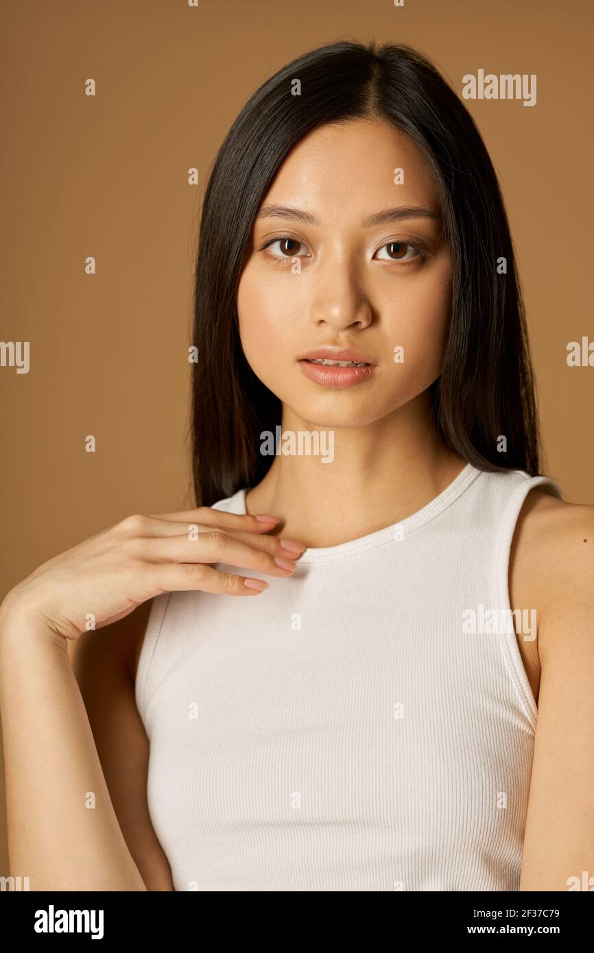 Retrato de una atractiva mujer joven de raza mixta con piel perfecta mirando la cámara mientras posan aislados sobre fondo marrón claro Foto de stock
