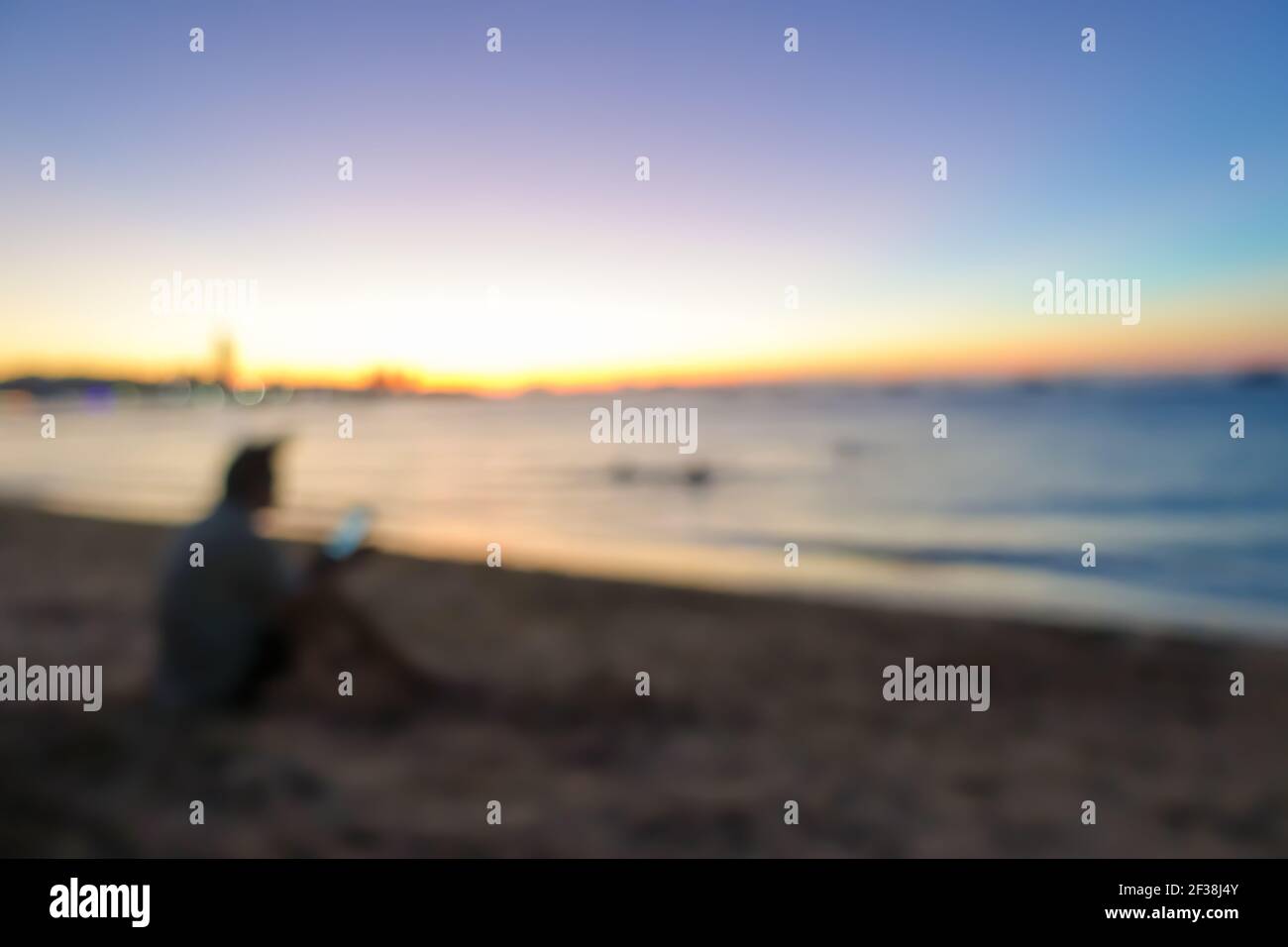 La imagen borrosa de un hombre sentado en la playa en el crepúsculo, se puede utilizar para el fondo Foto de stock
