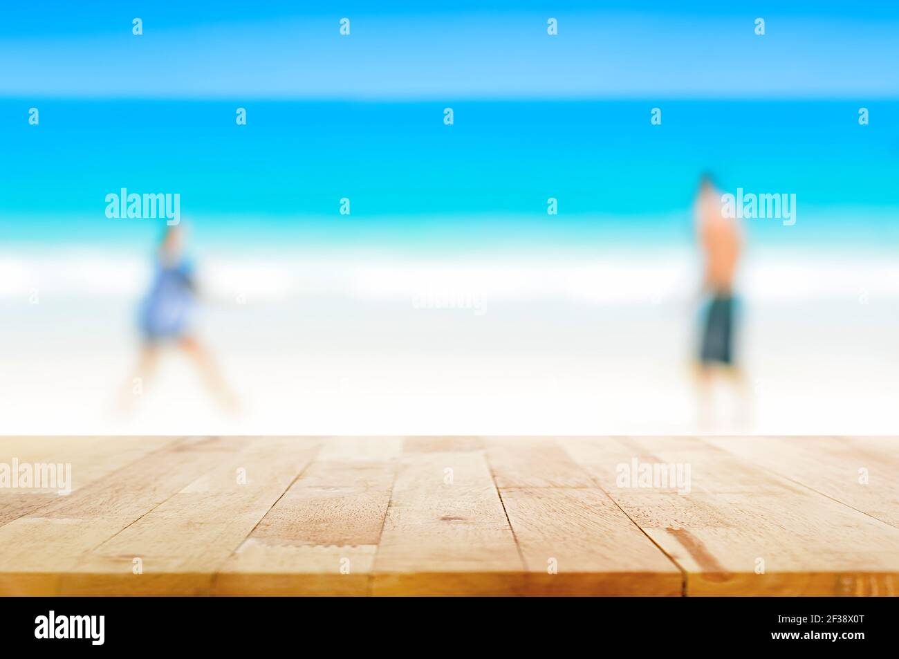 Mesa de madera sobre fondo borroso de dos personas jugando en la playa - se puede utilizar para mostrar o. montaje de sus productos Foto de stock