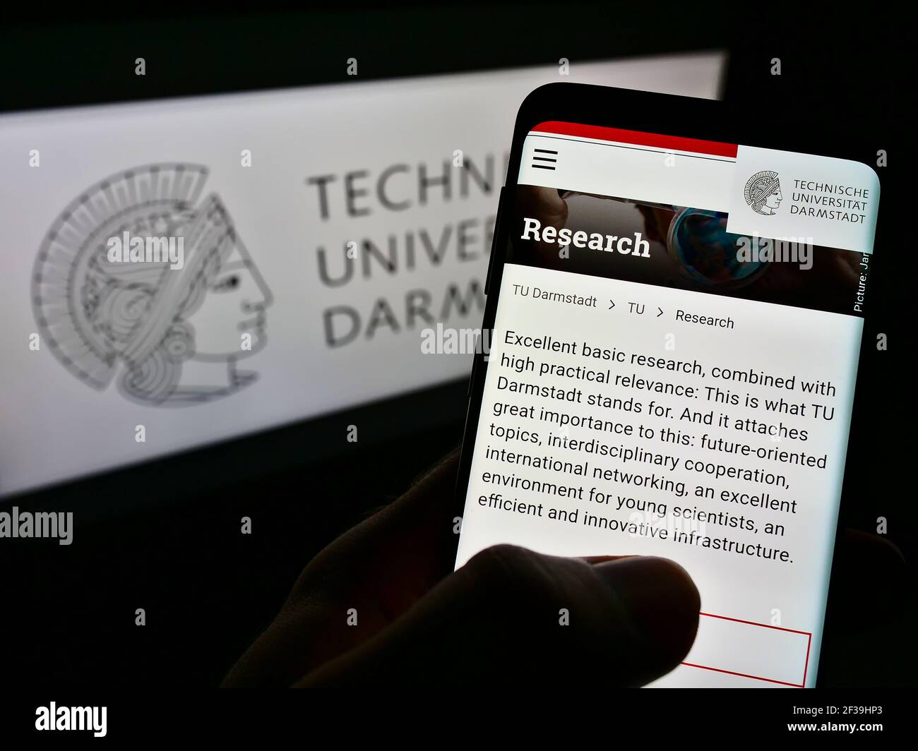 Persona que sostiene el teléfono celular con la página web de la Universidad Alemana de Tecnología de Darmstadt en la pantalla frente al logotipo. Enfoque en el centro de la pantalla del teléfono. Foto de stock