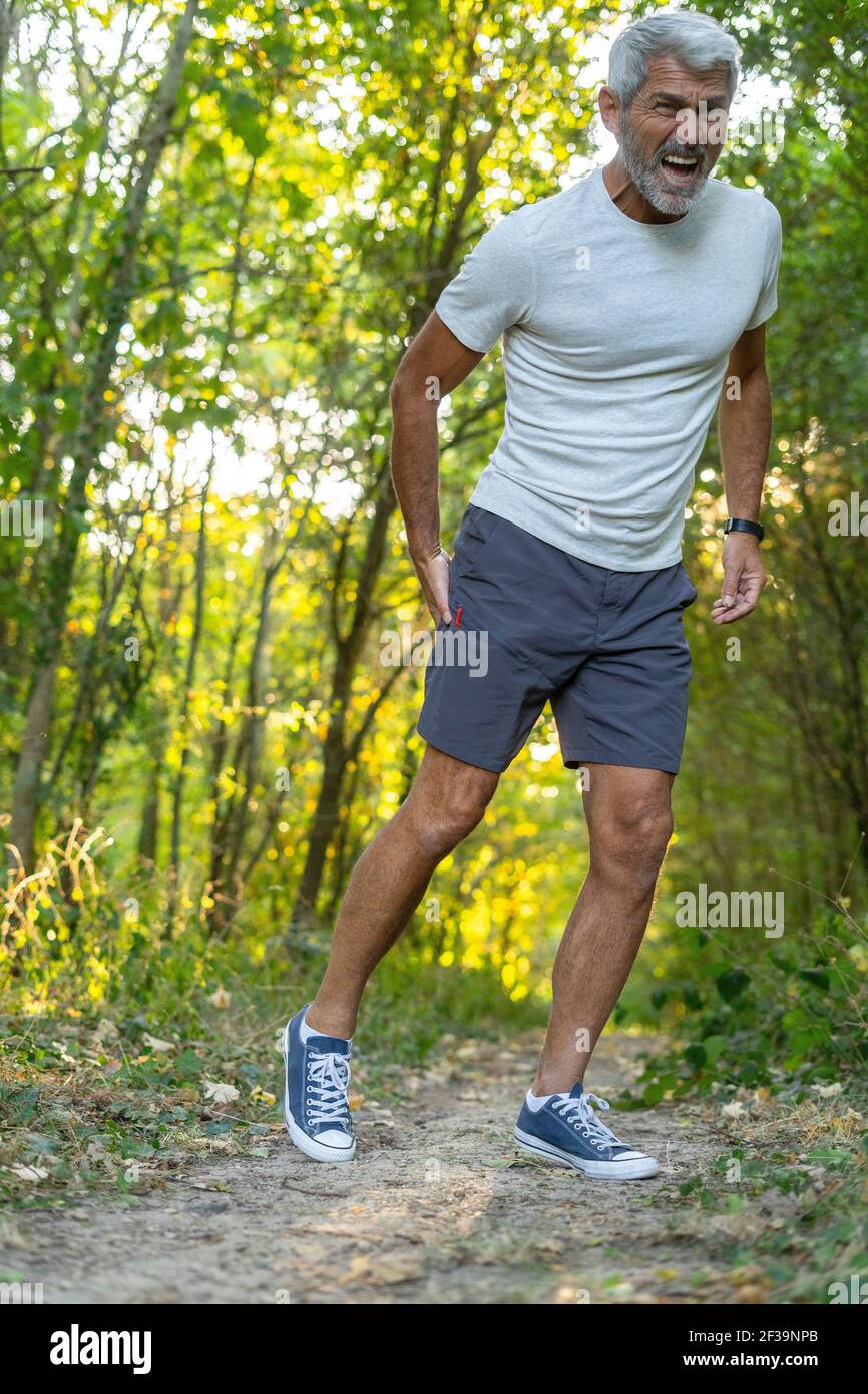 Hombre maduro que sufre de dolor en el muslo mientras está de pie en el bosque Foto de stock