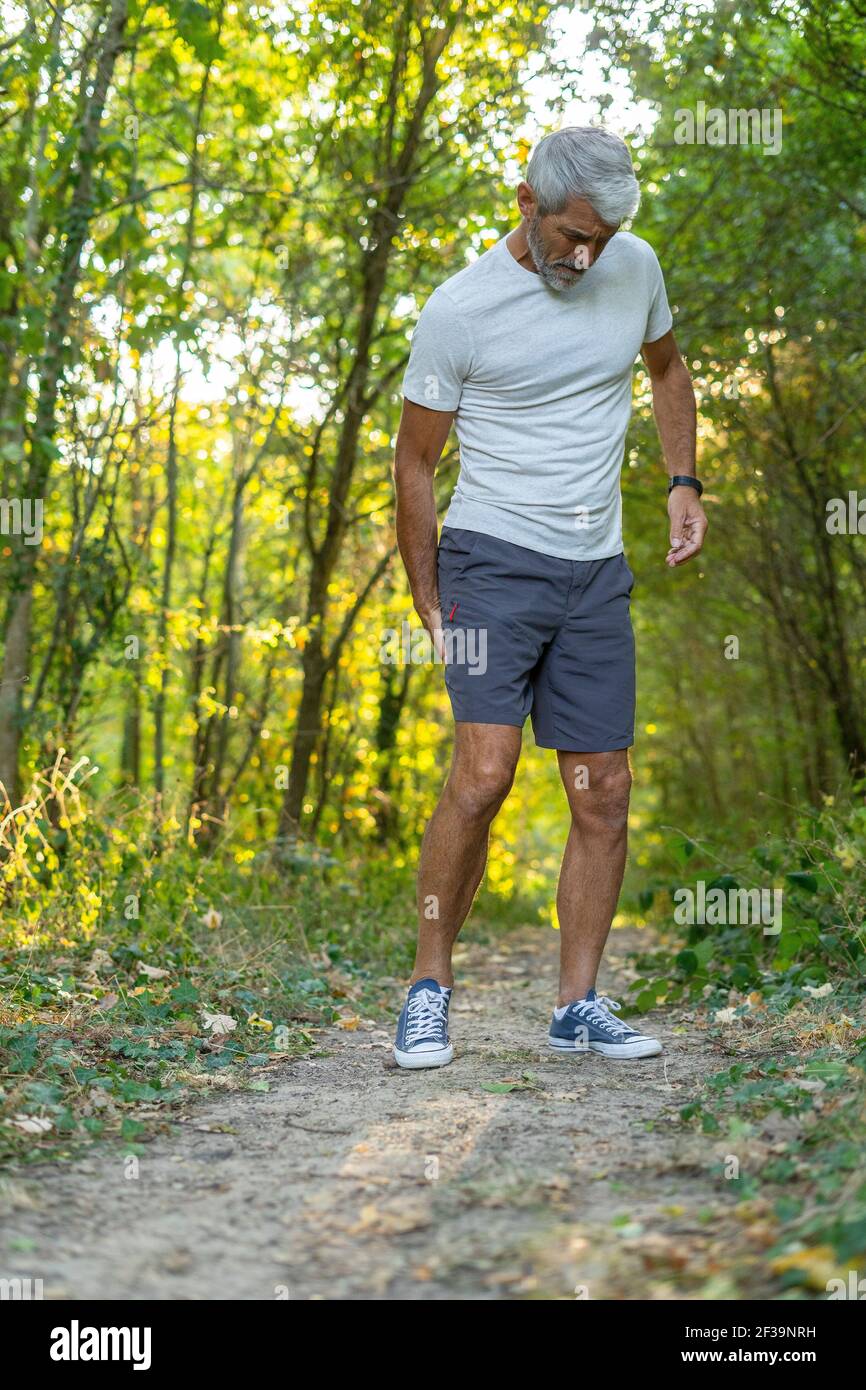 Hombre maduro que sufre de dolor en el muslo mientras está de pie en el bosque Foto de stock