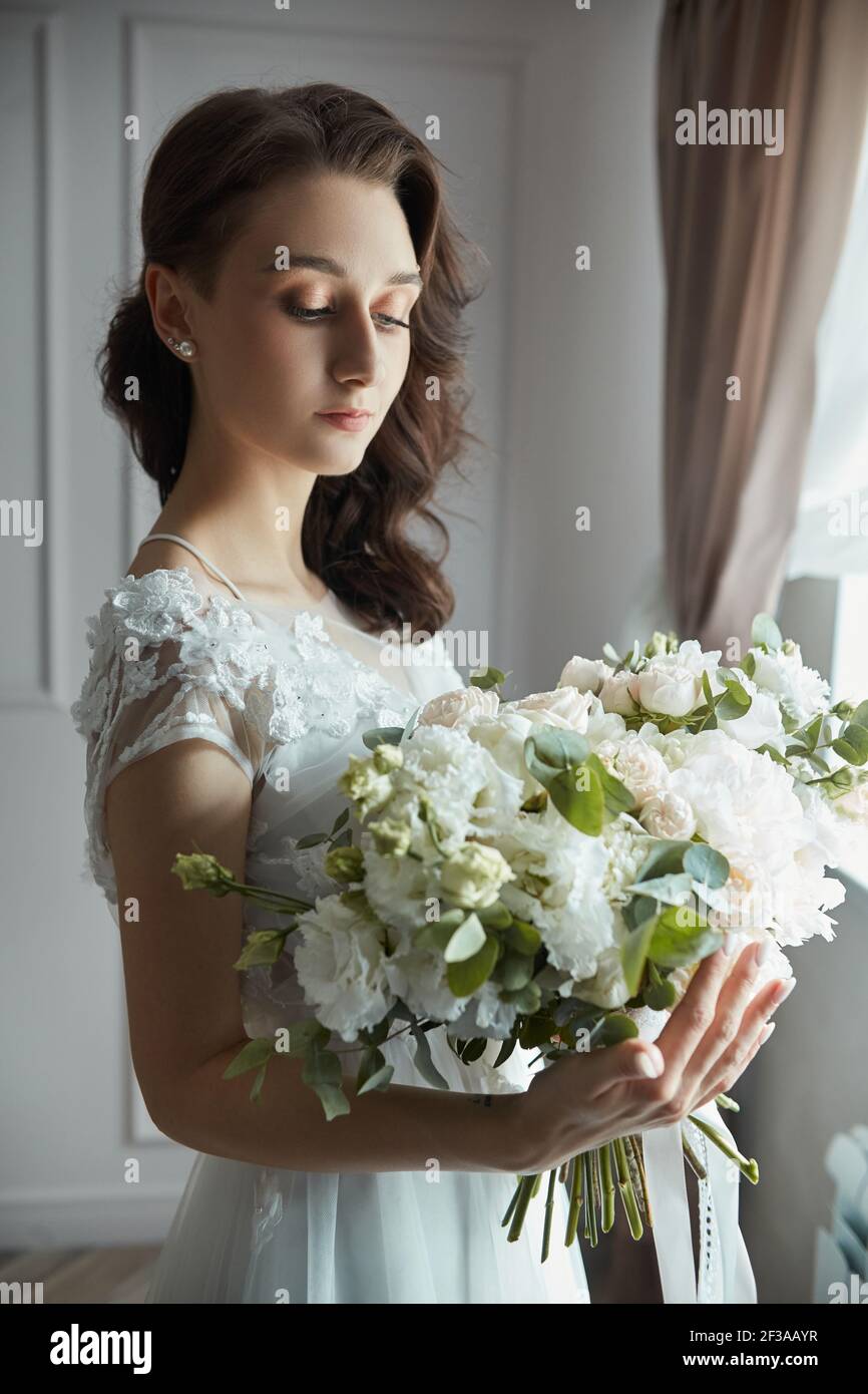 Mañana de la novia. Una mujer hermosa se está preparando para una boda,  maquillaje natural y un peinado chic. El peignoir blanco y el vestido de la  boda Fotografía de stock -