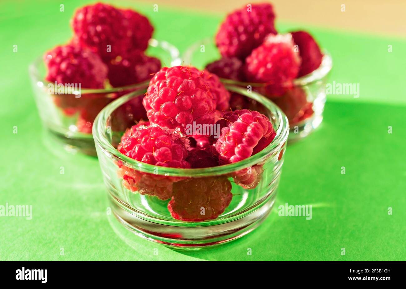 Frambuesas congeladas de cerca en tazas de vidrio sobre un fondo amarillo verde de primer plano. Alimentos saludables veganos, dieta, antioxidantes de bayas y vitaminas Foto de stock