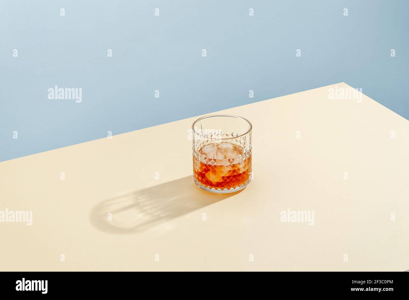 Vidrio con Whiskey y cubitos de hielo en la mesa sobre fondo azul. Estilo isométrico moderno. Concepto creativo. Foto de stock