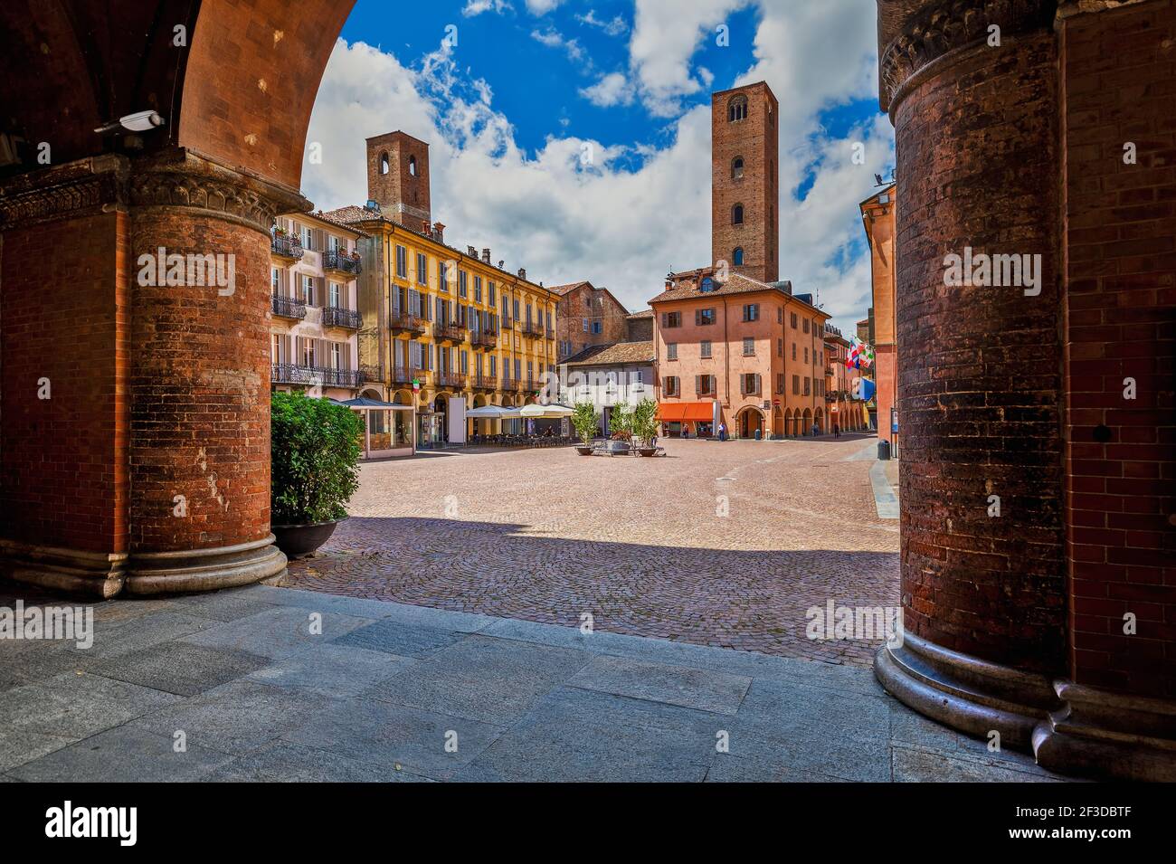 Vista de la plaza de la ciudad adoquinada entre casas antiguas y torres medievales bajo el hermoso cielo en Alba, Piamonte, Norte de Italia. Foto de stock