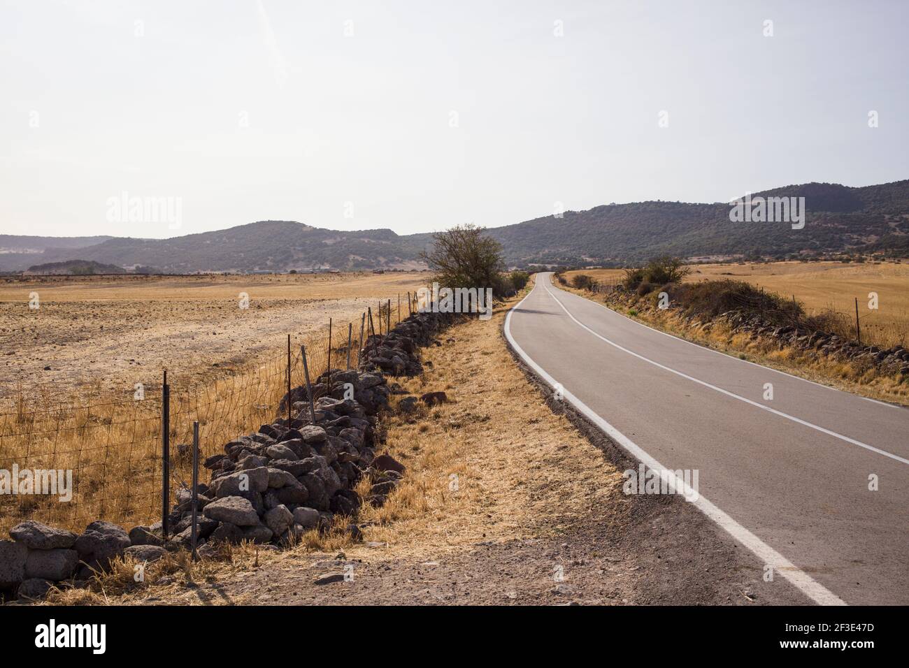 Carretera vacía en Cerdeña. Paisaje con cielos azules campos secos y montañas en la distancia. Foto de stock