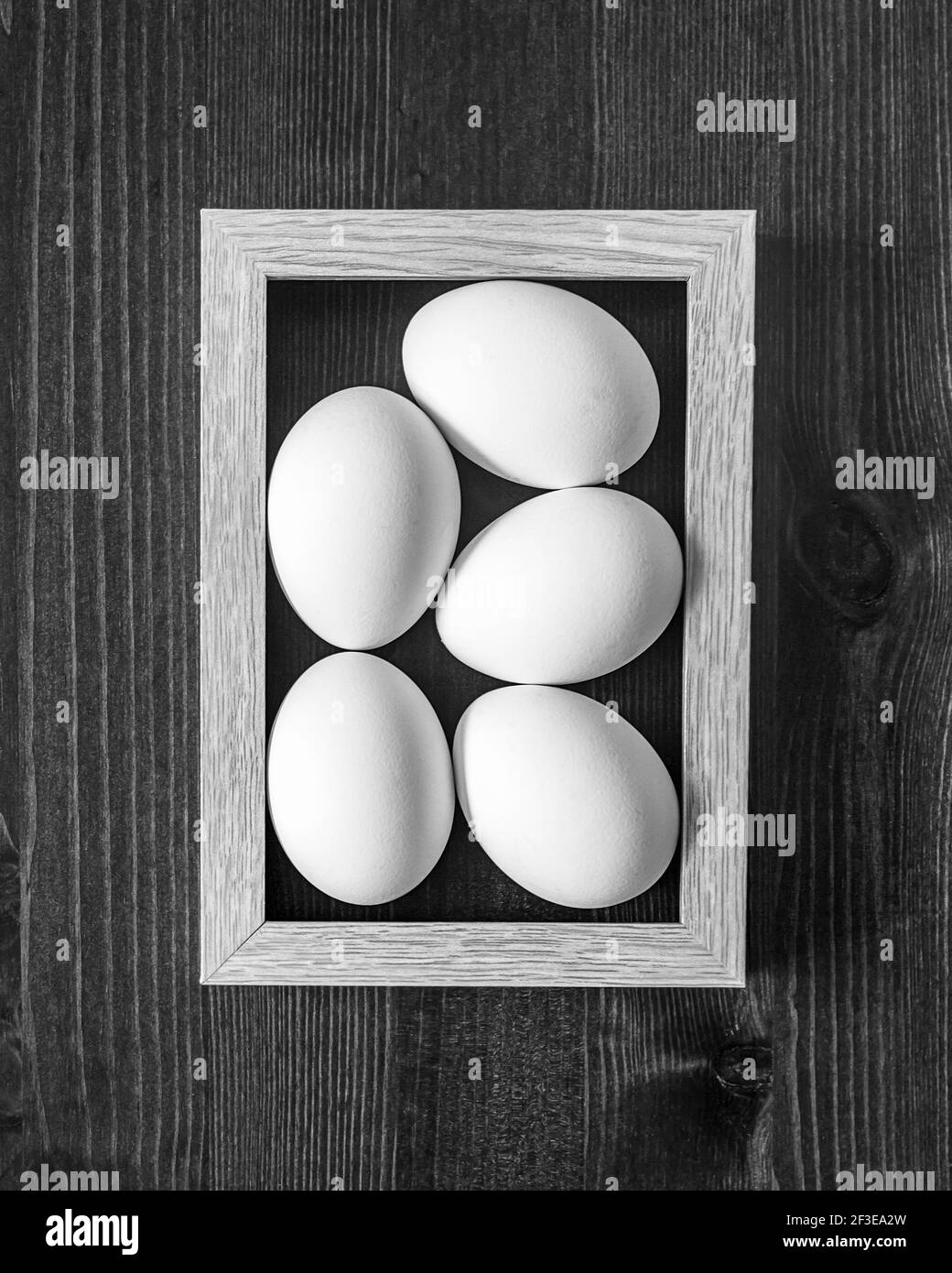 El concepto de un alimento natural sano simple. Pollo, huevos blancos y frescos en un marco sobre un fondo de madera. Foto de comida en blanco y negro, vista superior. Comp Foto de stock