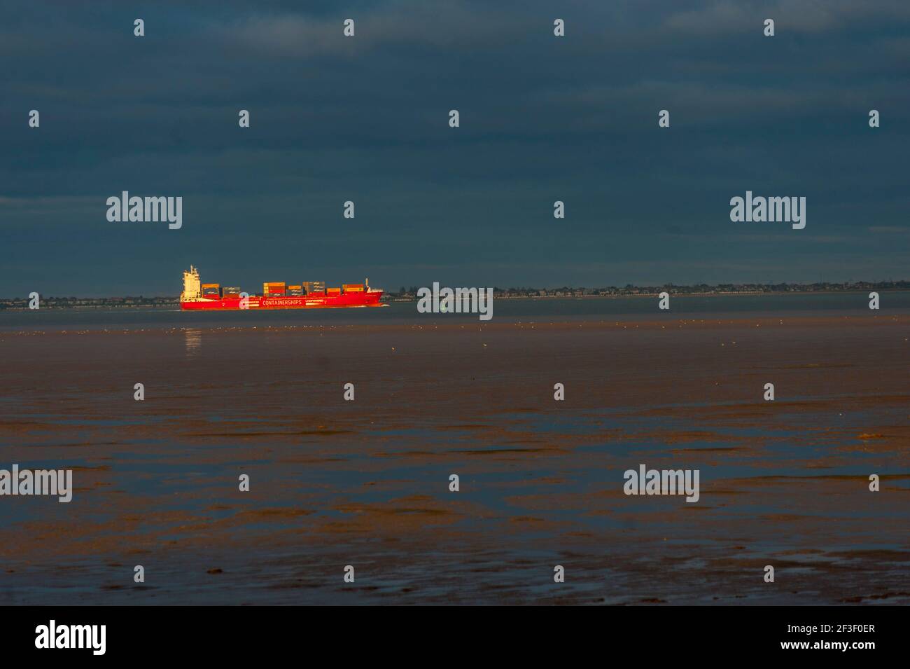 Un barco de contenedores navegando por el Támesis desde el paseo marítimo de Grain Kent. Con la costa de Essex detrás Foto de stock